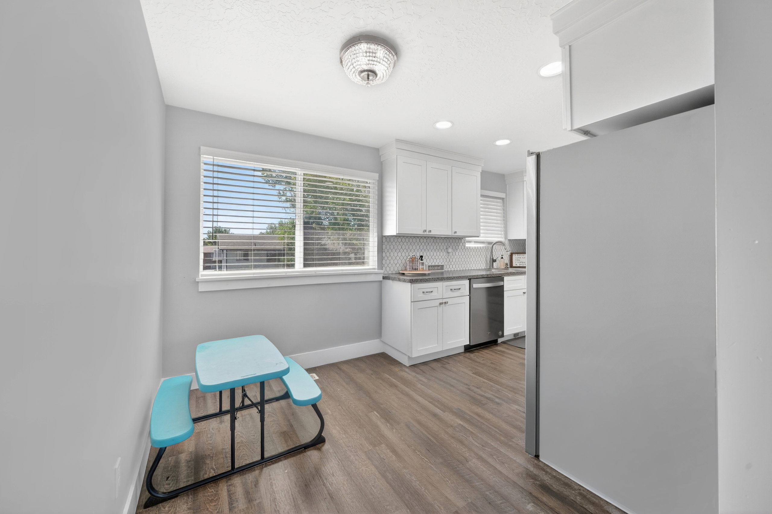 Bright kitchen area featuring white cabinetry, stainless steel appliances, wood-finish flooring, a patterned tile backsplash, and recessed lighting