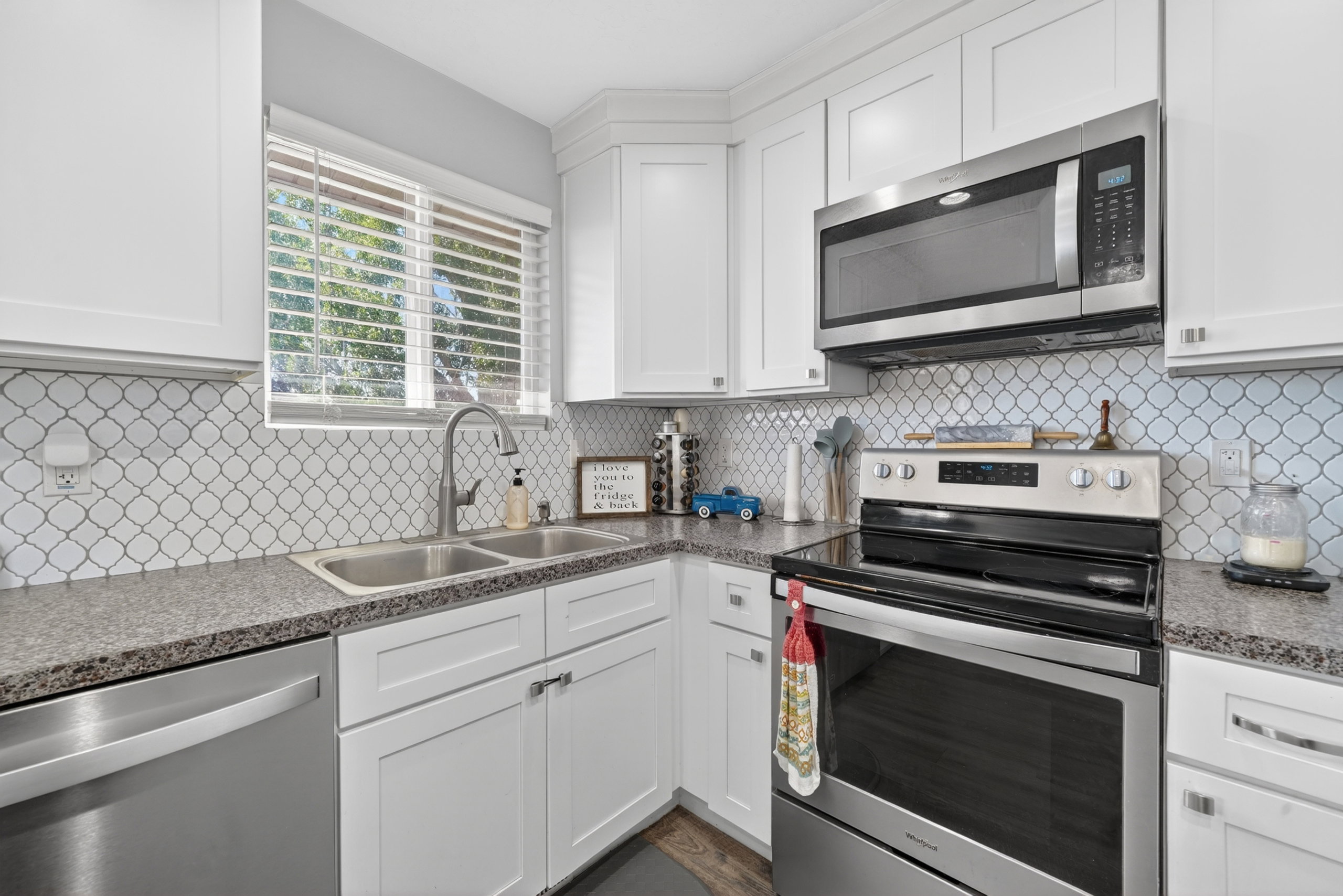 Kitchen featuring white cabinetry, patterned tile backsplash, stainless steel appliances, a double basin sink, and stone-finish countertops