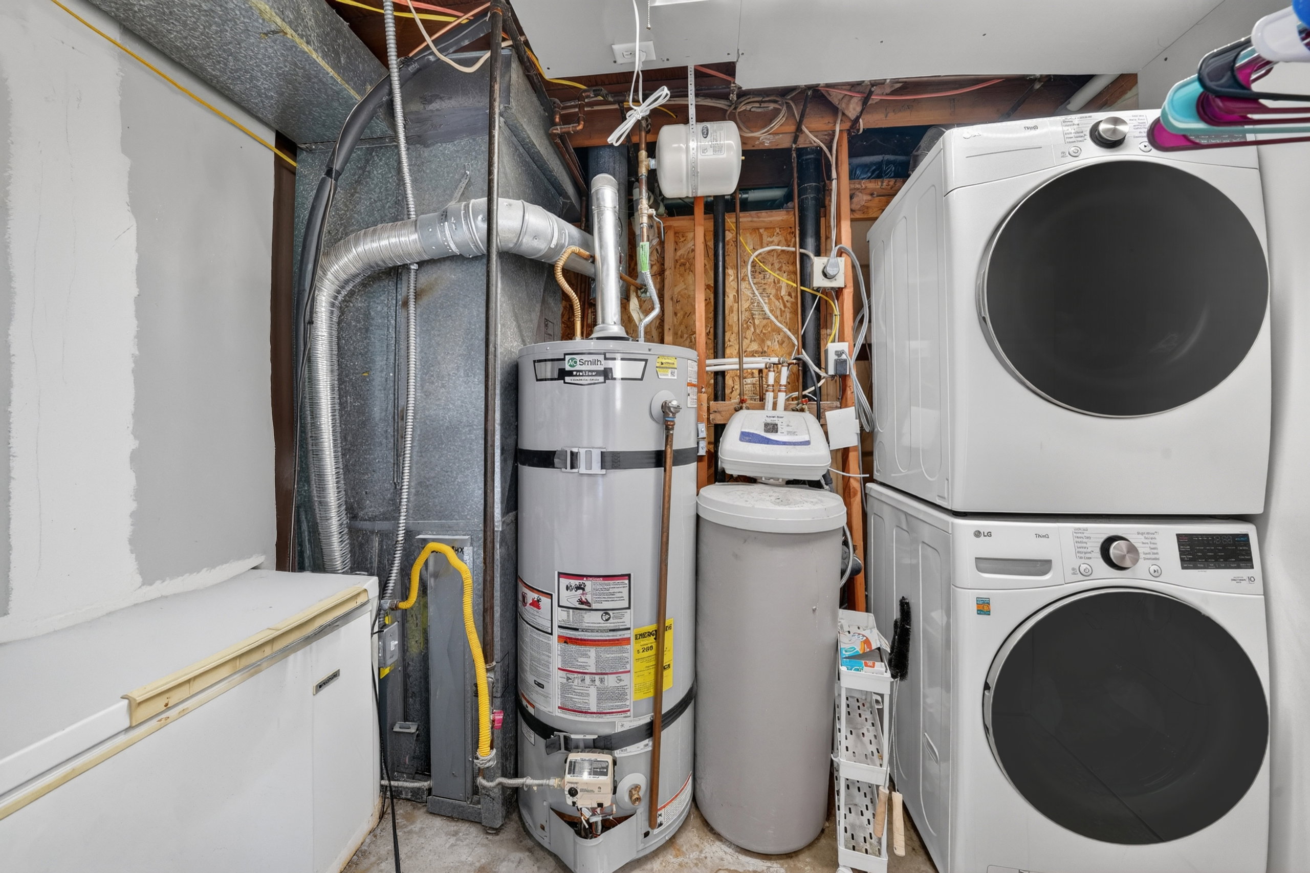 Laundry area featuring a stacked washer and dryer, water heater, water softener, and furnace