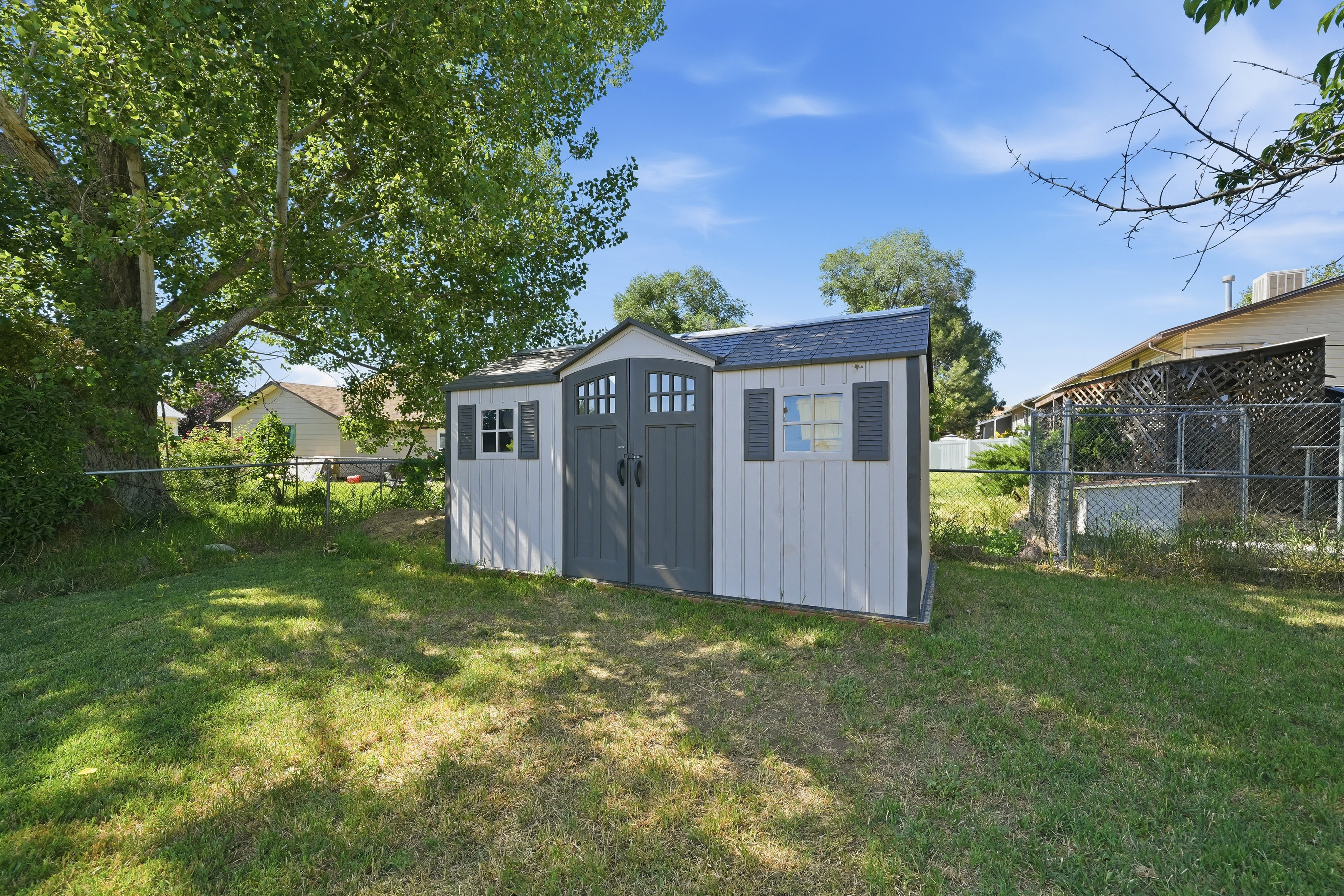 Detached storage shed with panel siding, double doors, two windows with shutters, and a shingled roof