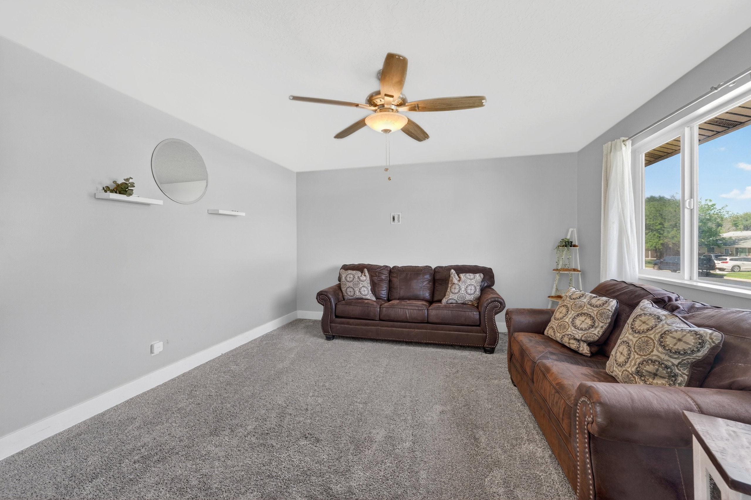 Spacious room featuring light gray wall paint, white trim, gray carpet flooring, and a ceiling fan with integrated lighting