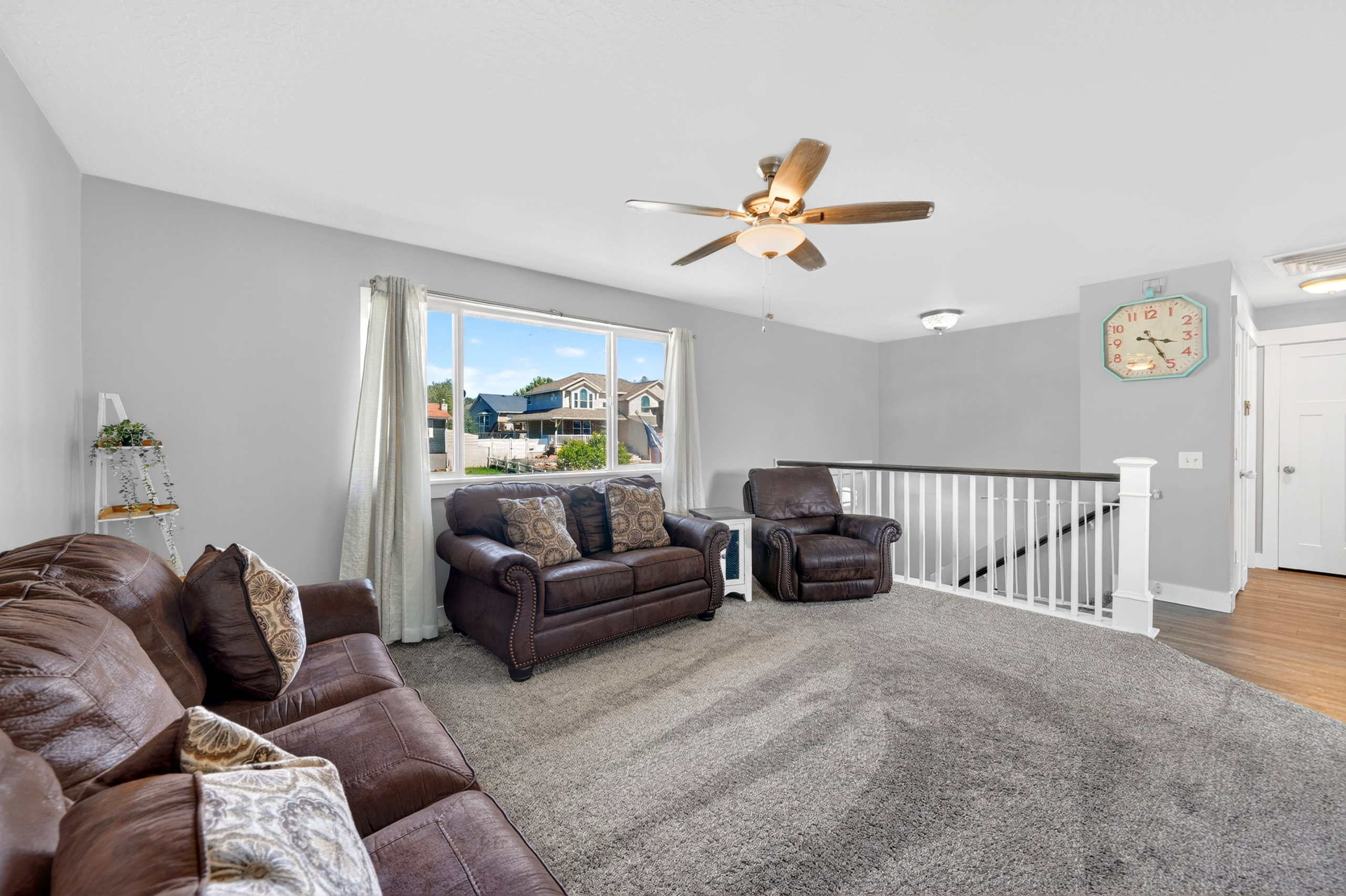 Spacious upper-level living area with ample natural light, soft gray carpeting, a multi-pane window, and a built-in ceiling fan with integrated lighting