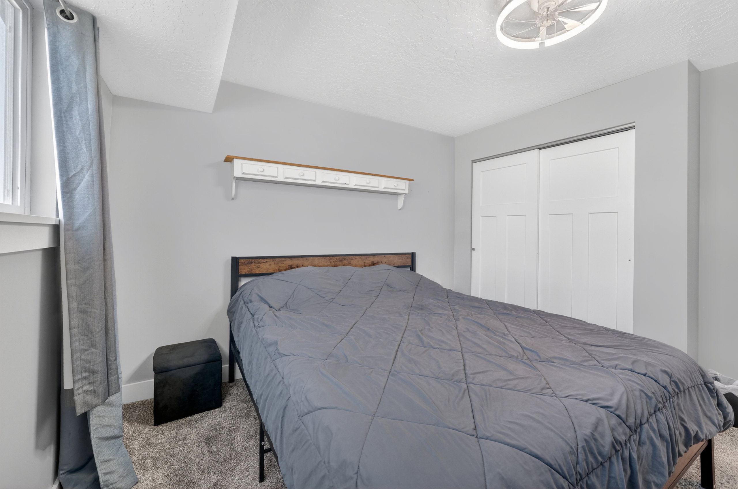 Carpeted bedroom featuring a window with white trim, a built-in decorative shelf with small drawers, and a ceiling-mounted fan light fixture