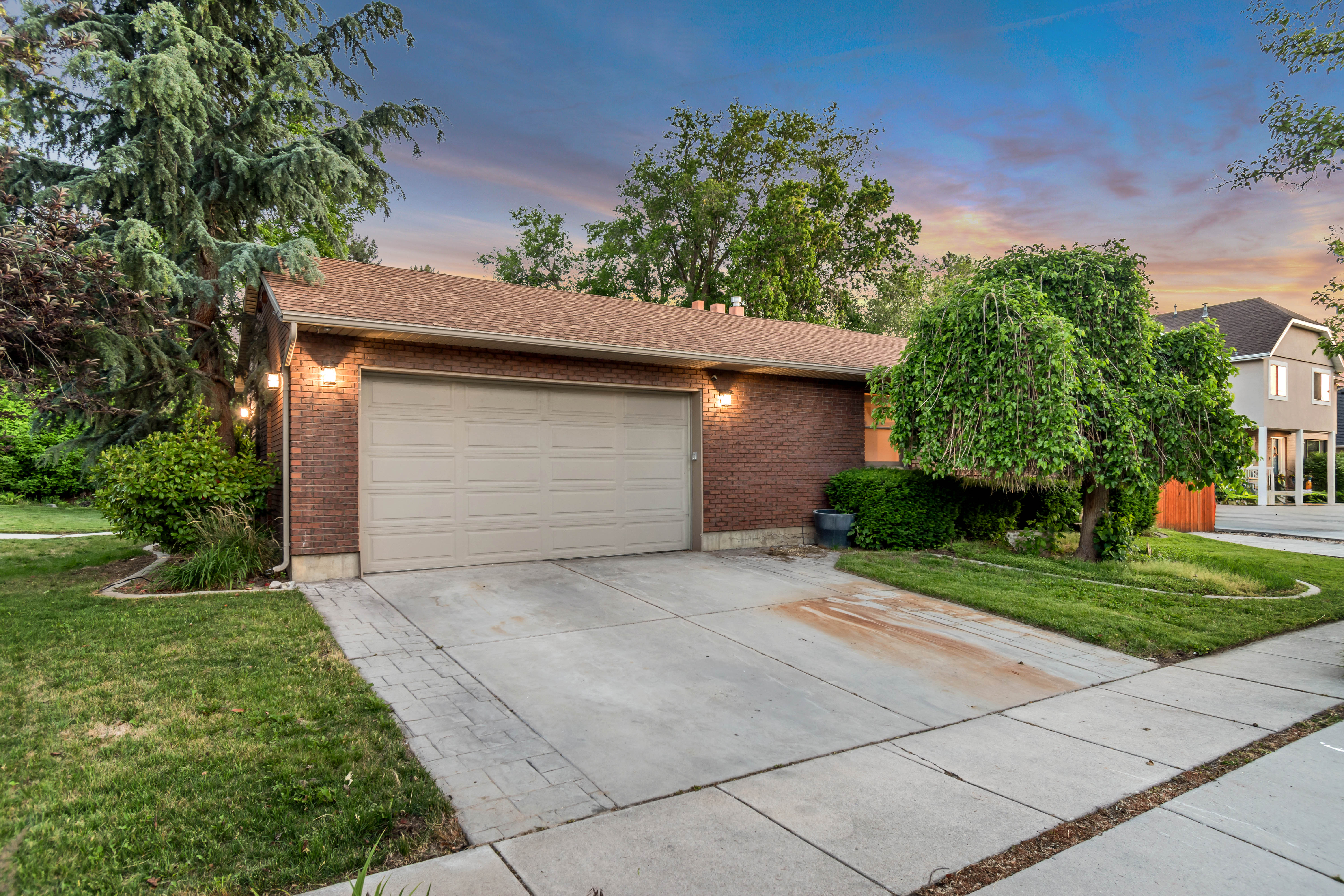 Brick exterior with a two-car garage and concrete driveway featuring paver accents