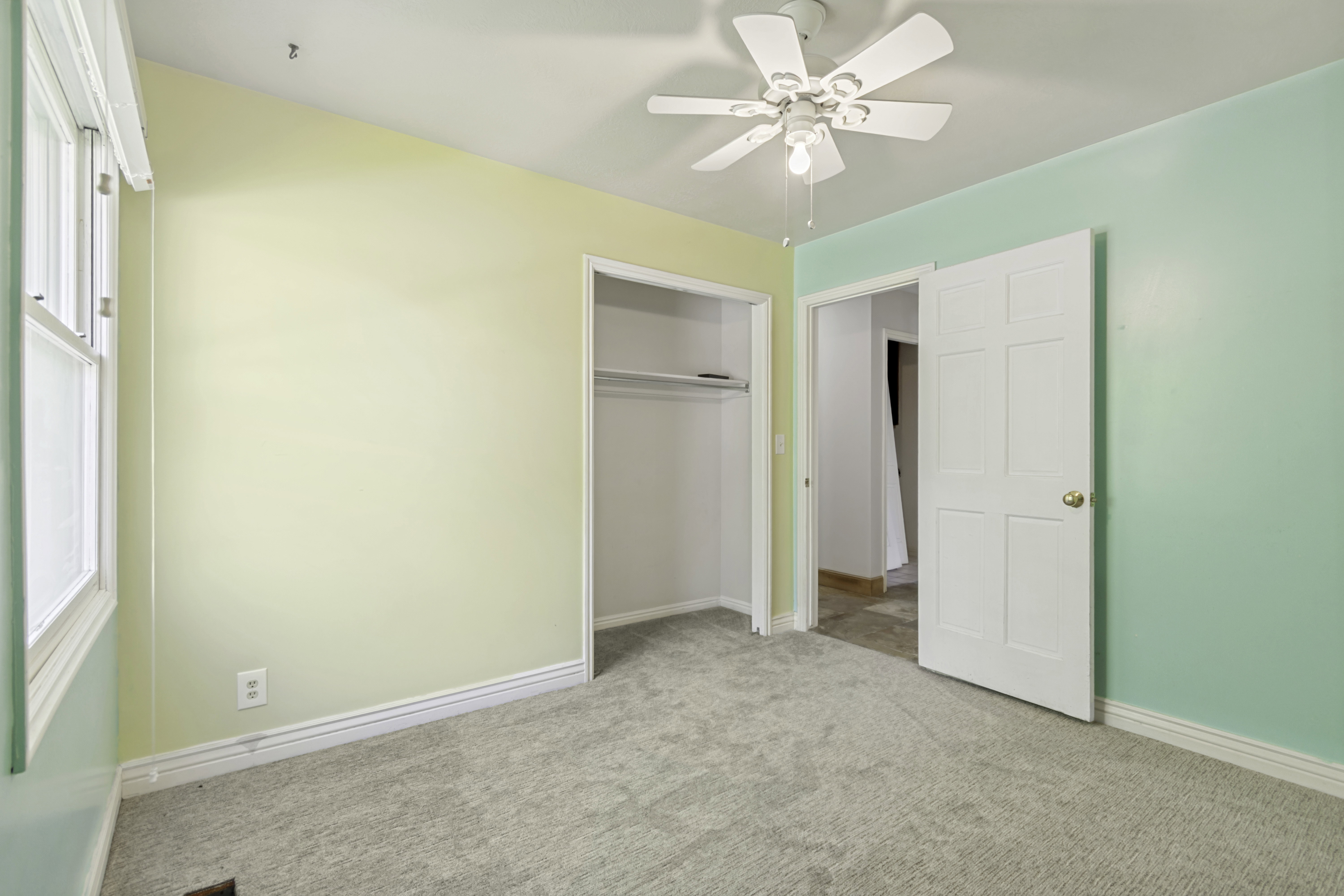 Carpeted room featuring a ceiling fan with integrated lighting, a window, a single-panel door, and a built-in closet with shelving
