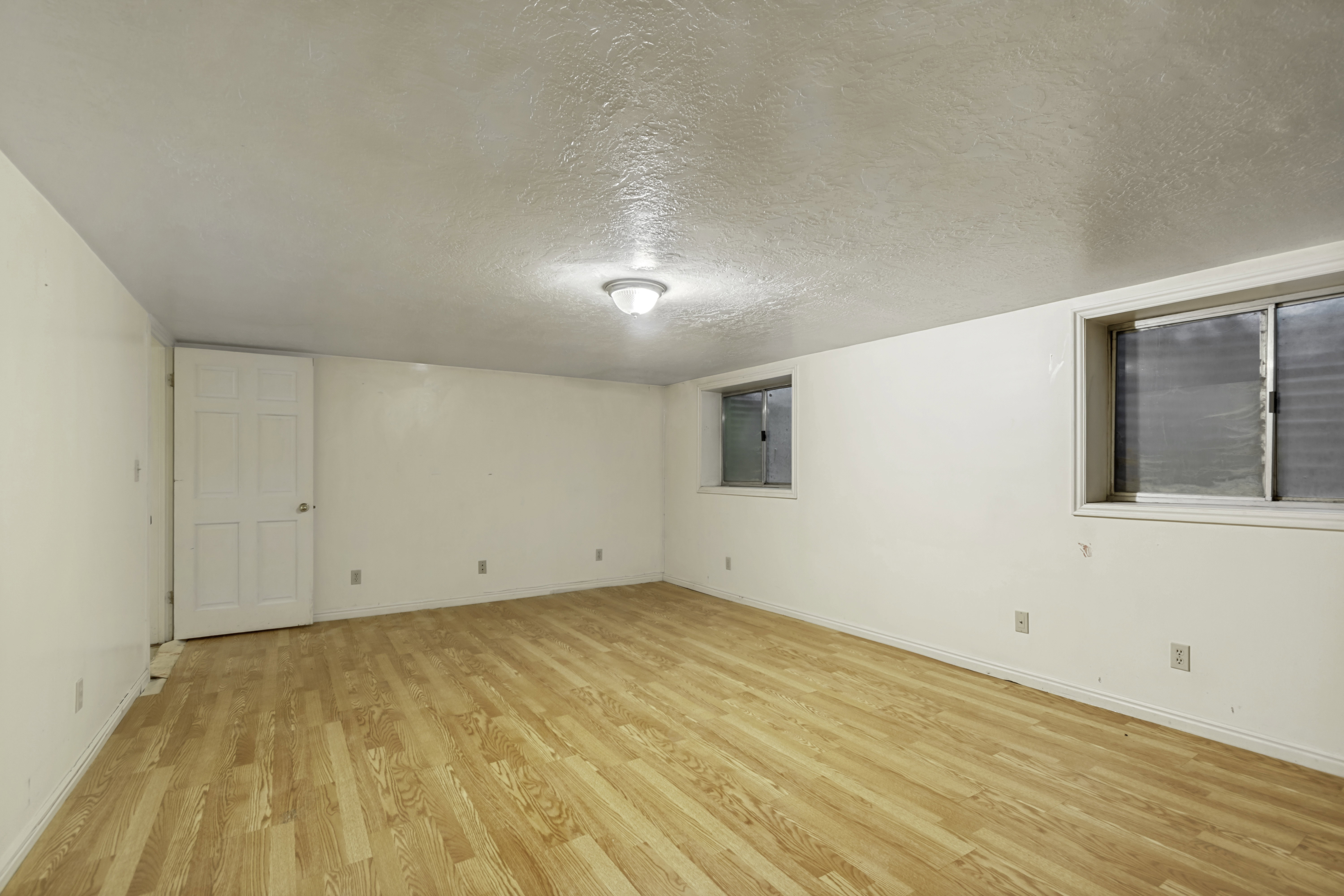 Spacious room featuring wood-finish flooring, white walls, and a ceiling-mounted light fixture