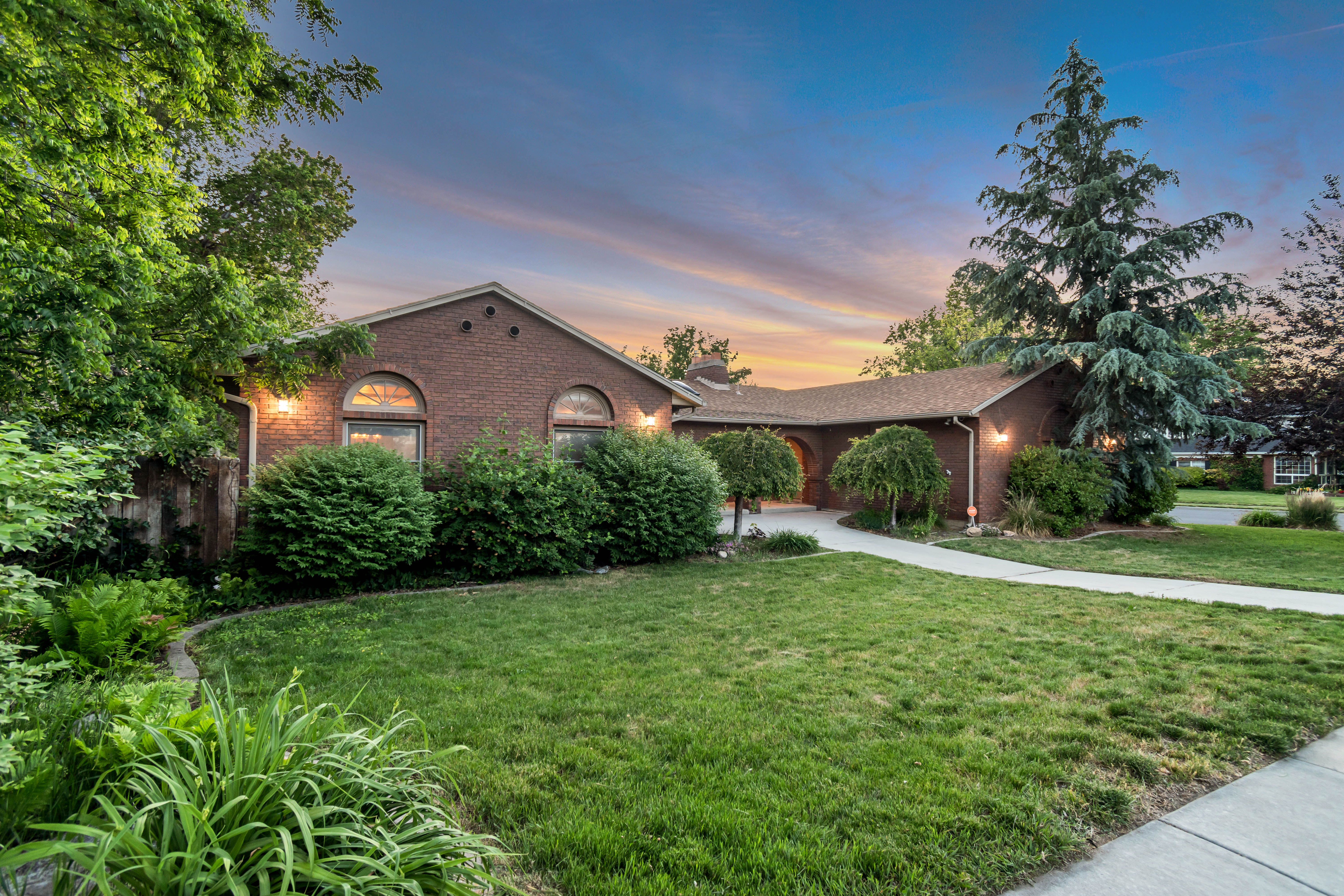 Brick facade residence featuring arched windows, mature landscaping, a paved walkway, and a manicured lawn