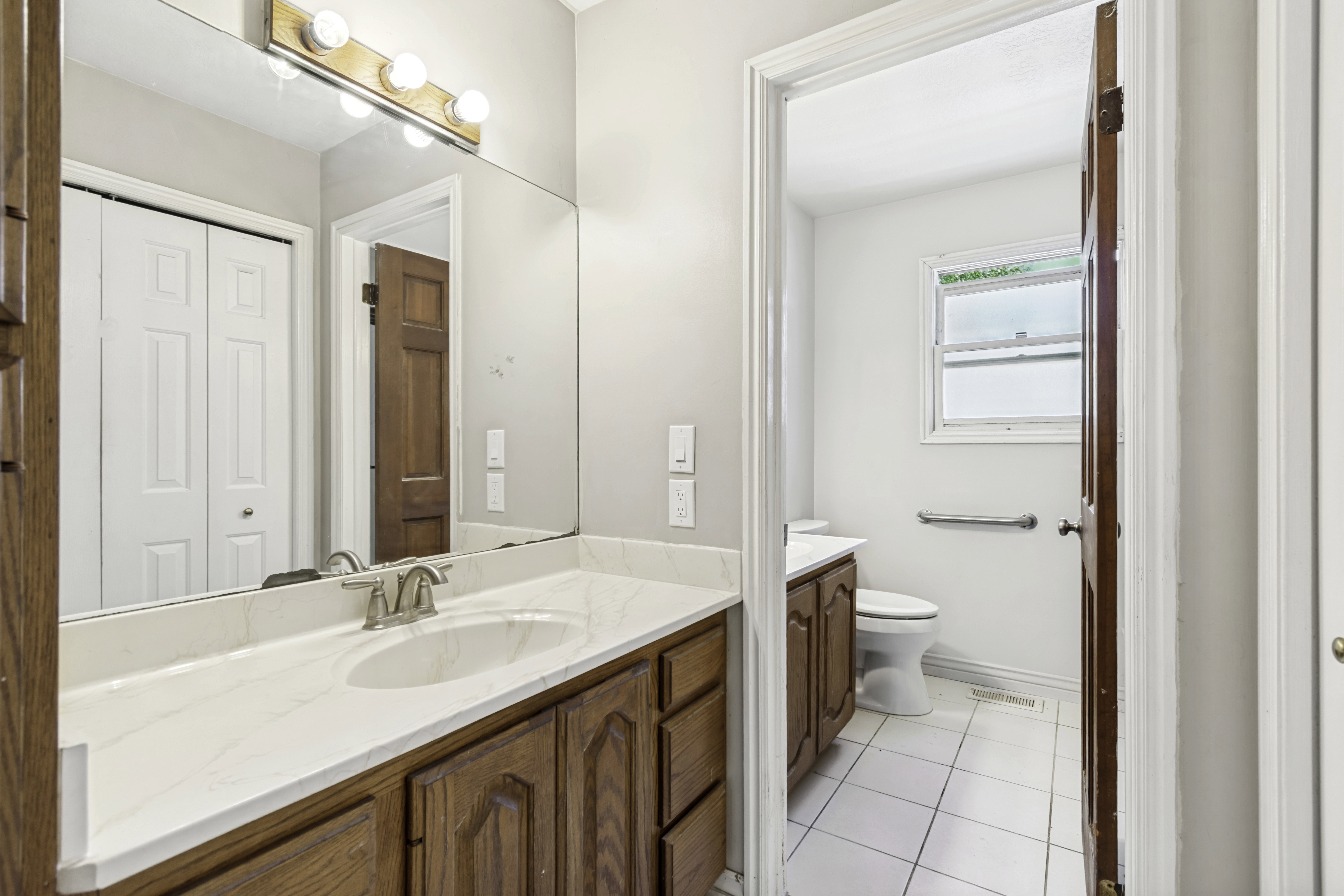 Bathroom vanity featuring a white countertop with an integrated sink, brushed nickel faucet, and wood-finish cabinetry