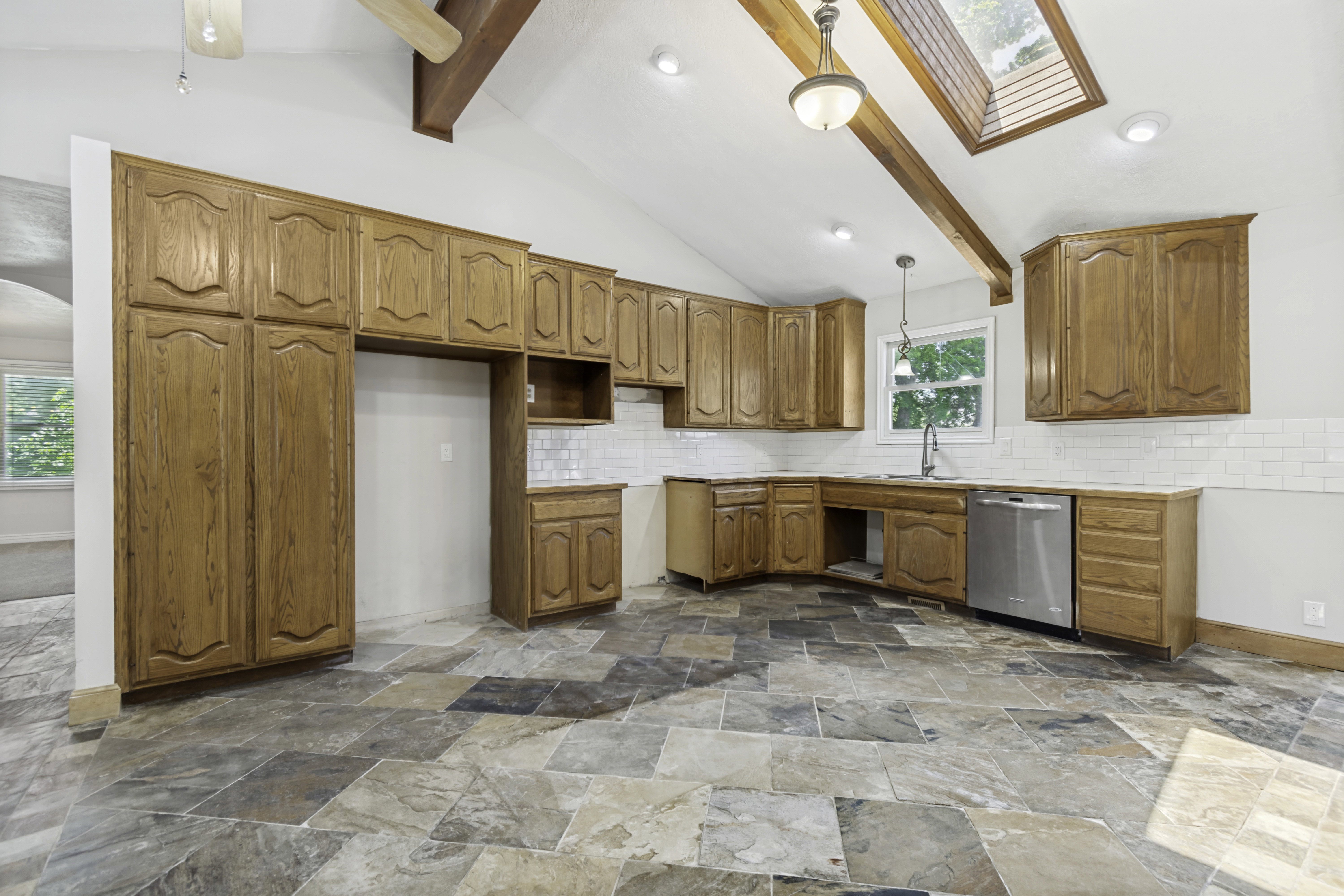 Spacious kitchen featuring a vaulted ceiling with exposed wood beams, skylight, recessed lighting, and a hanging pendant light fixture