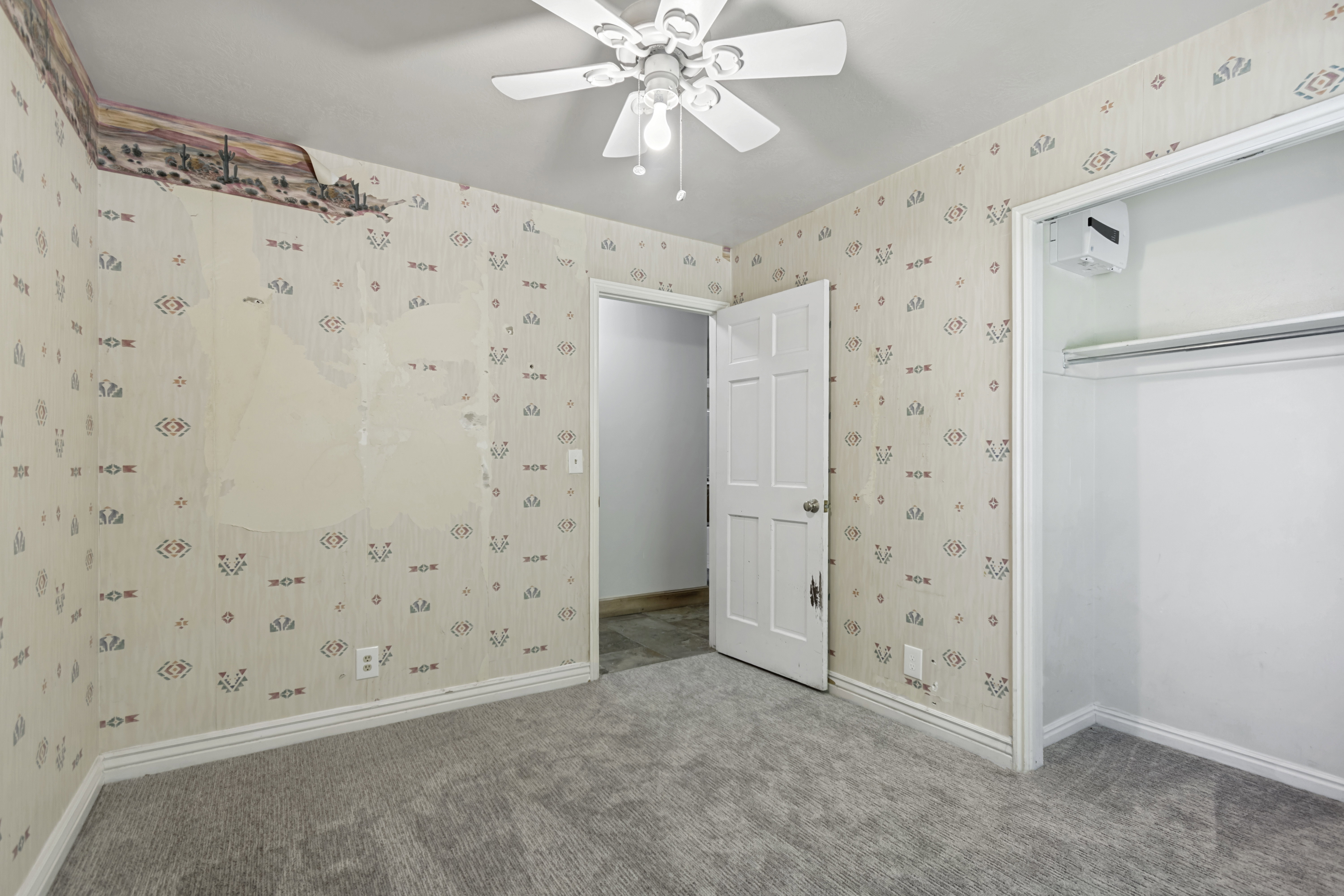 Carpeted room featuring a ceiling fan with integrated lighting, patterned wallpaper, white trim, and a built-in closet with a hanging rod
