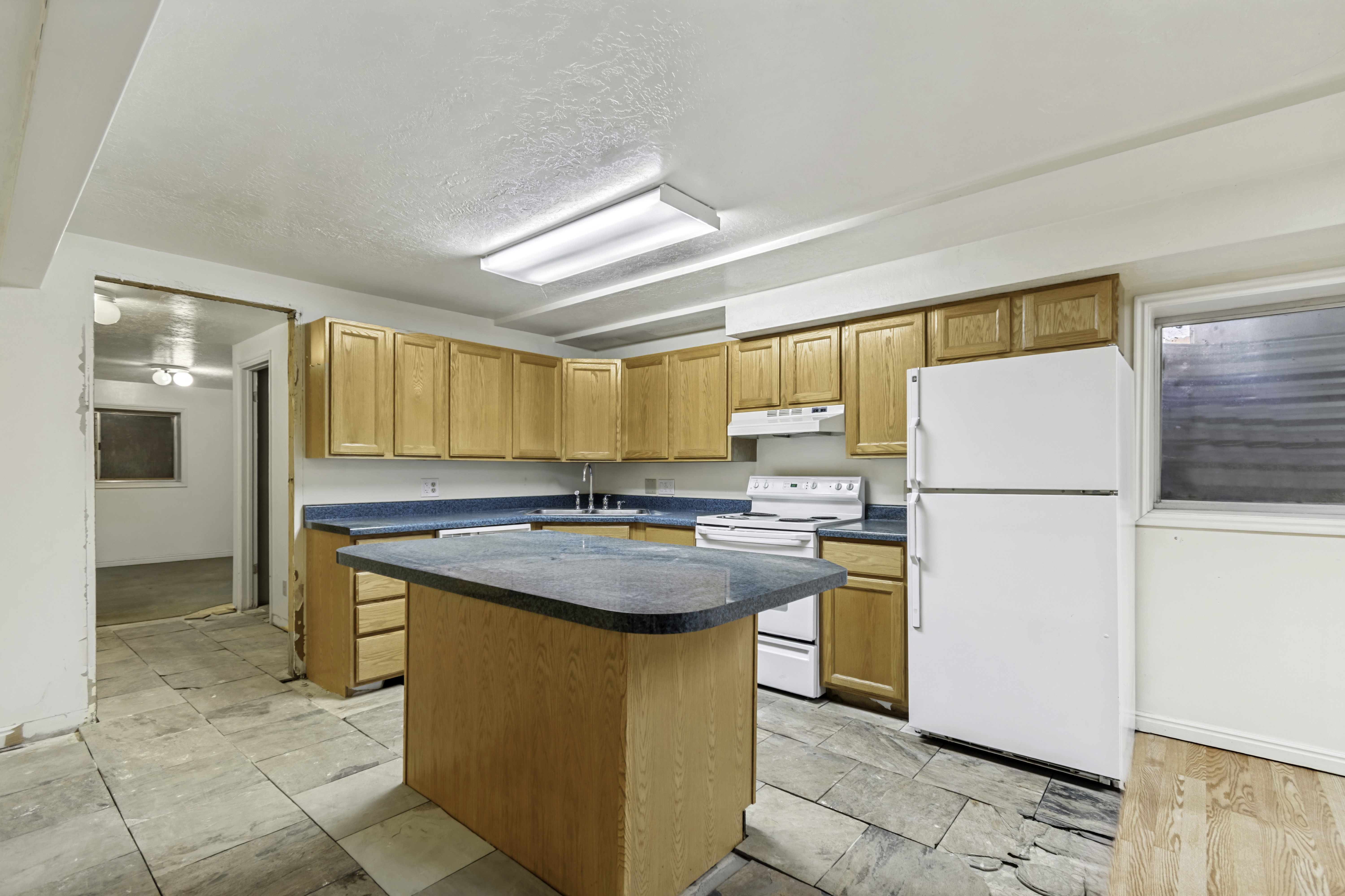 Kitchen featuring an island with a dark countertop, light wood cabinetry, white appliances, and tiled flooring