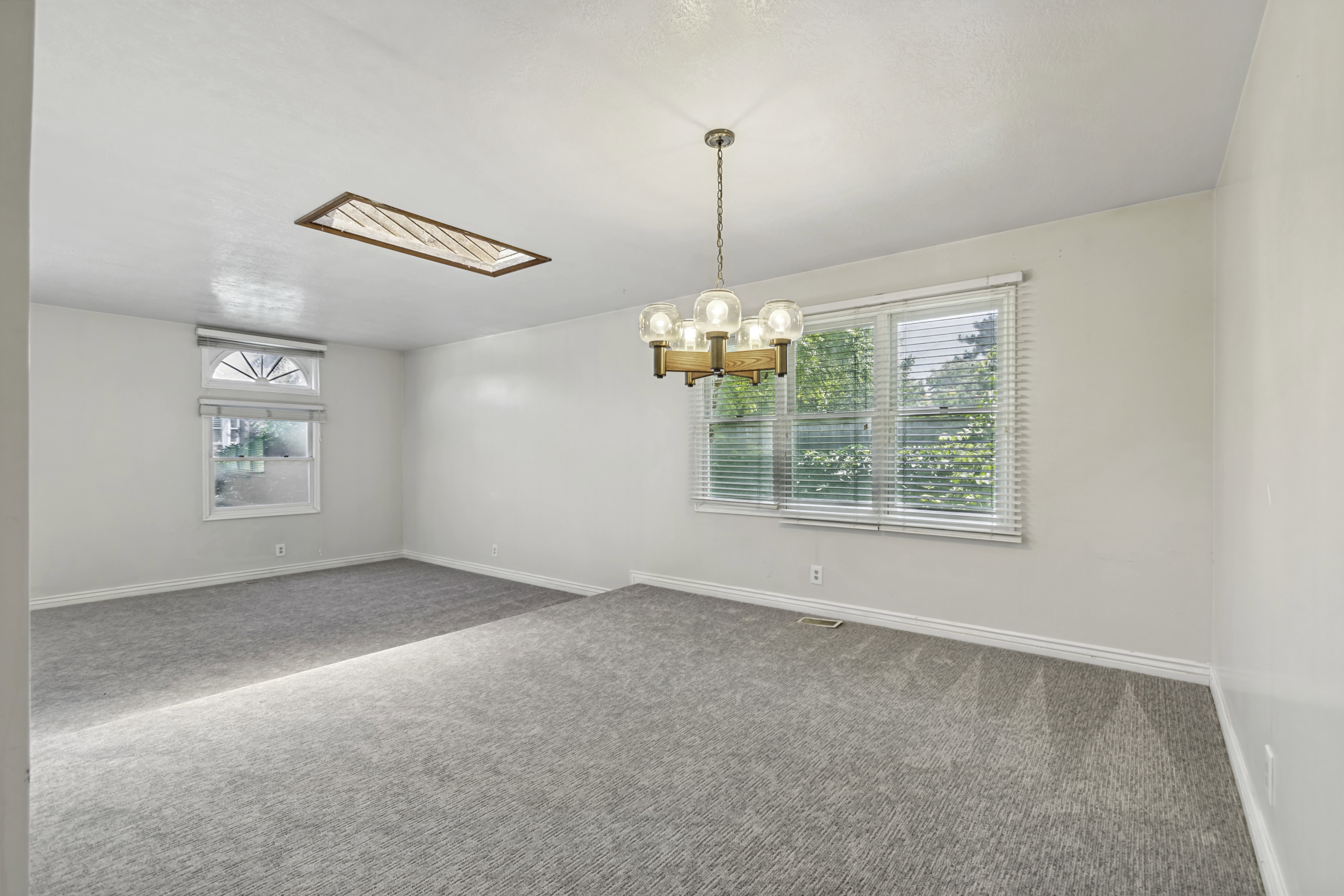 Spacious room featuring light gray carpeting, neutral wall finishes, and a contemporary chandelier