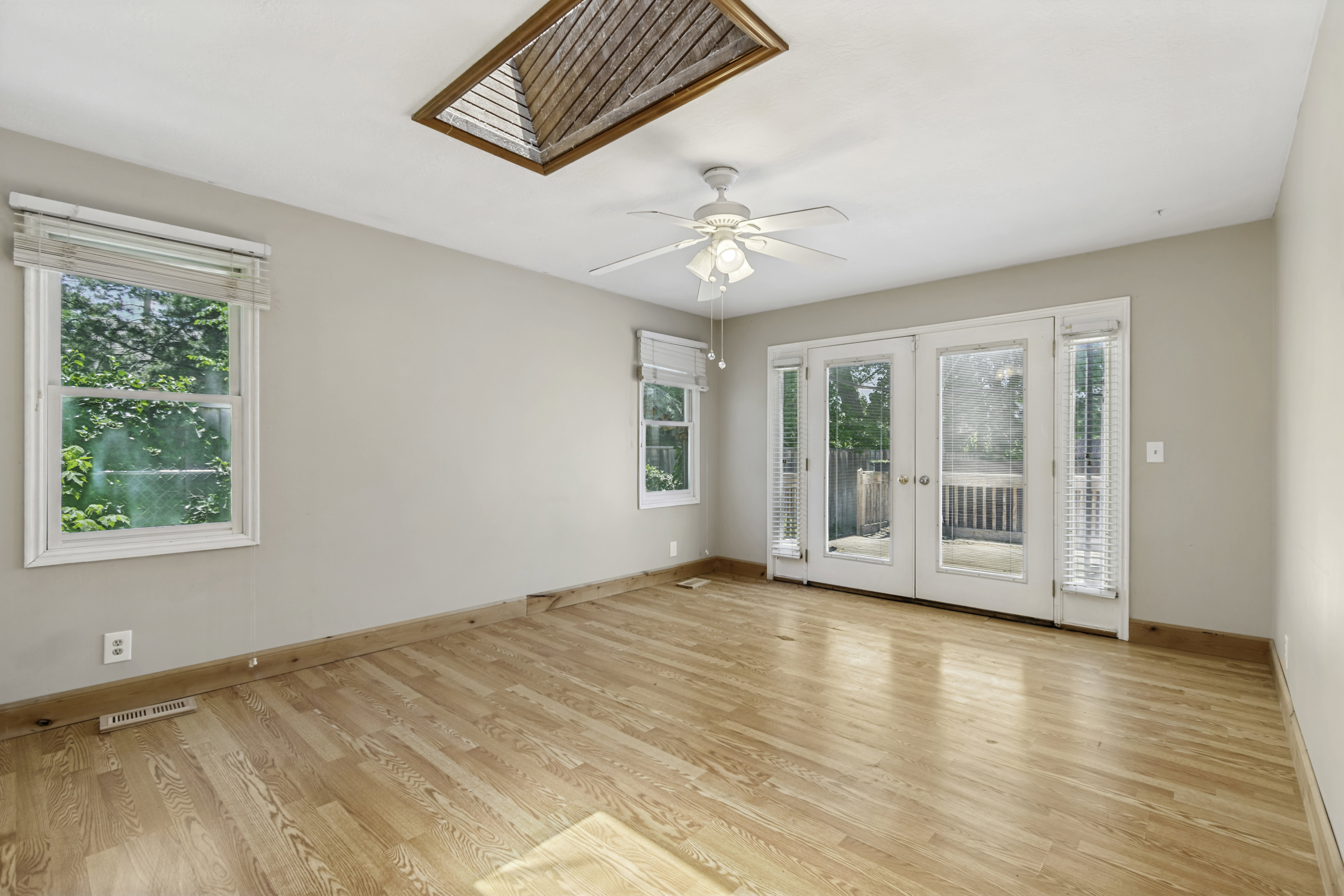 Room with wood-finish flooring, a ceiling fan, and a wood-slatted skylight