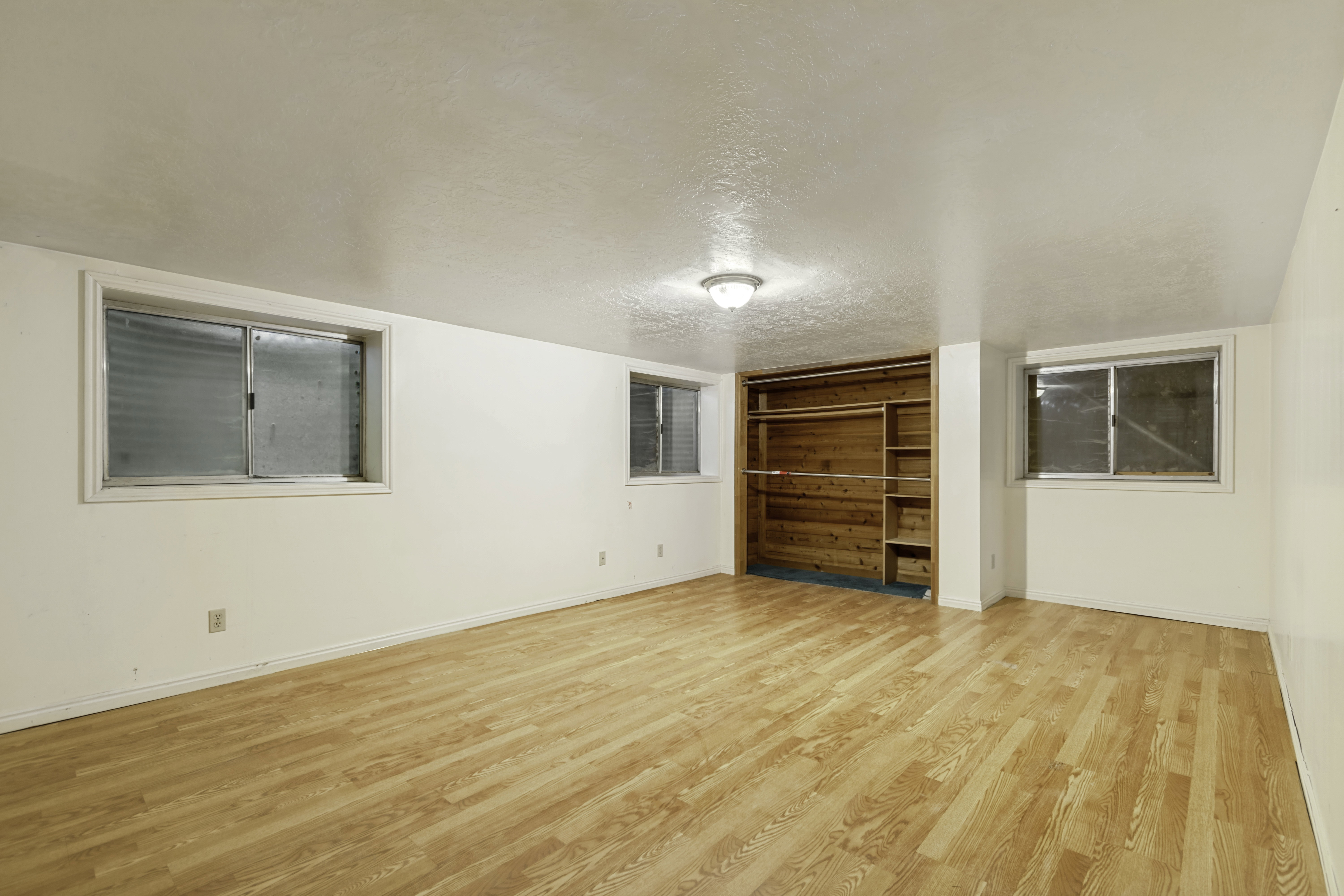 Spacious room featuring light wood-finish flooring, white walls, and multiple windows