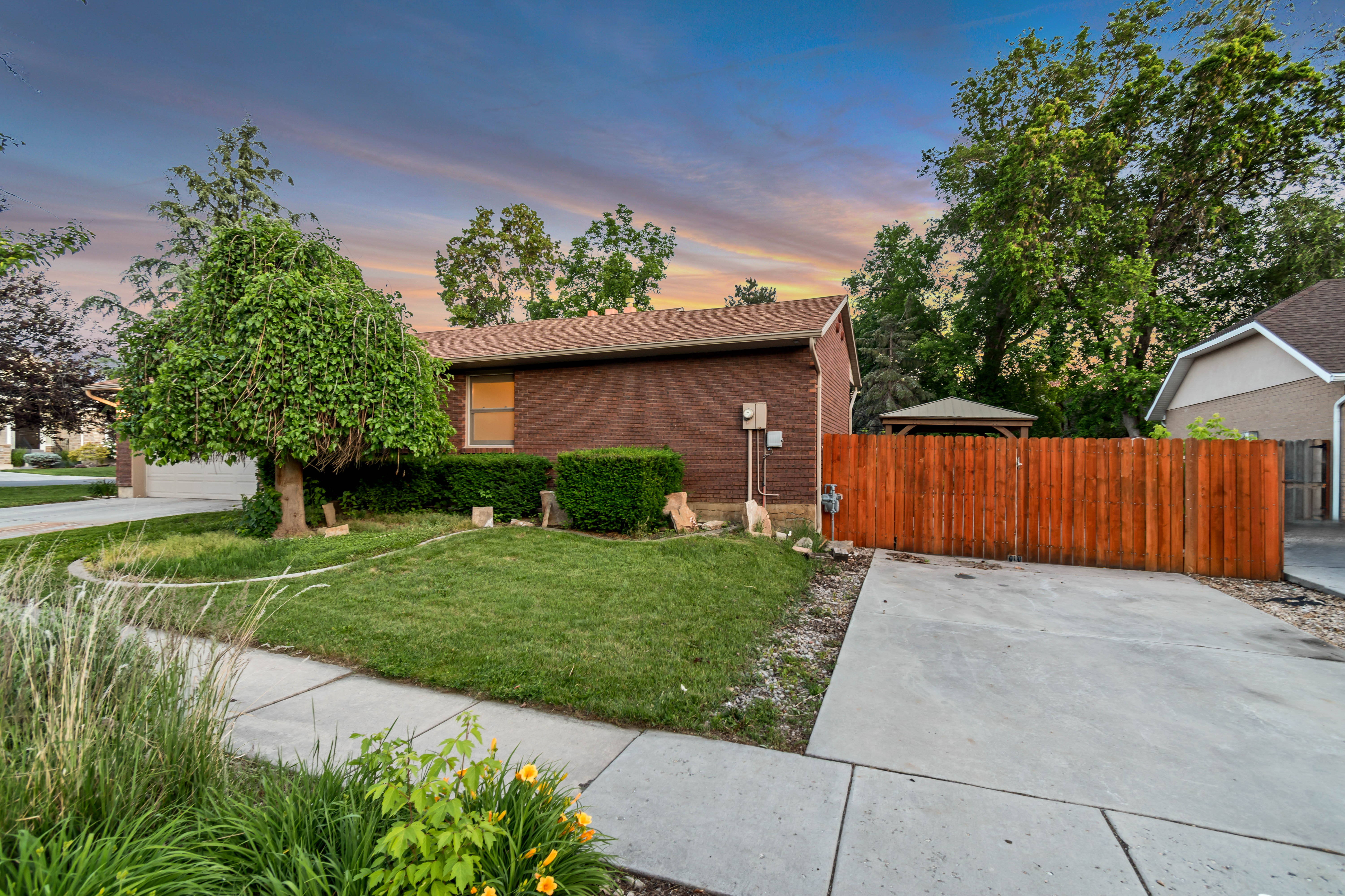 Brick exterior residence featuring a concrete driveway, a wood fence, and a gazebo