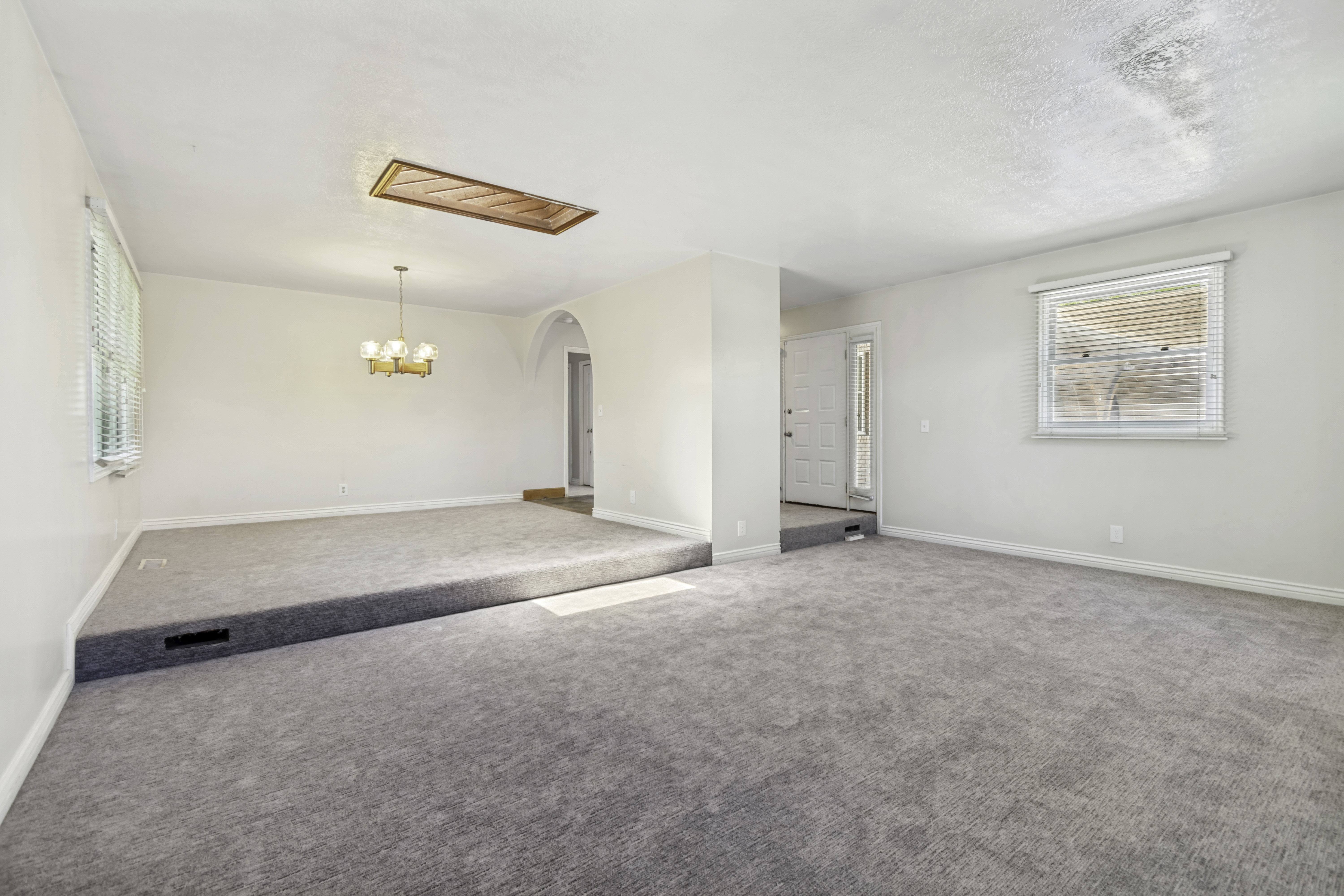 Spacious interior featuring two distinct carpeted floor levels, an arched doorway, and a brass-tone chandelier
