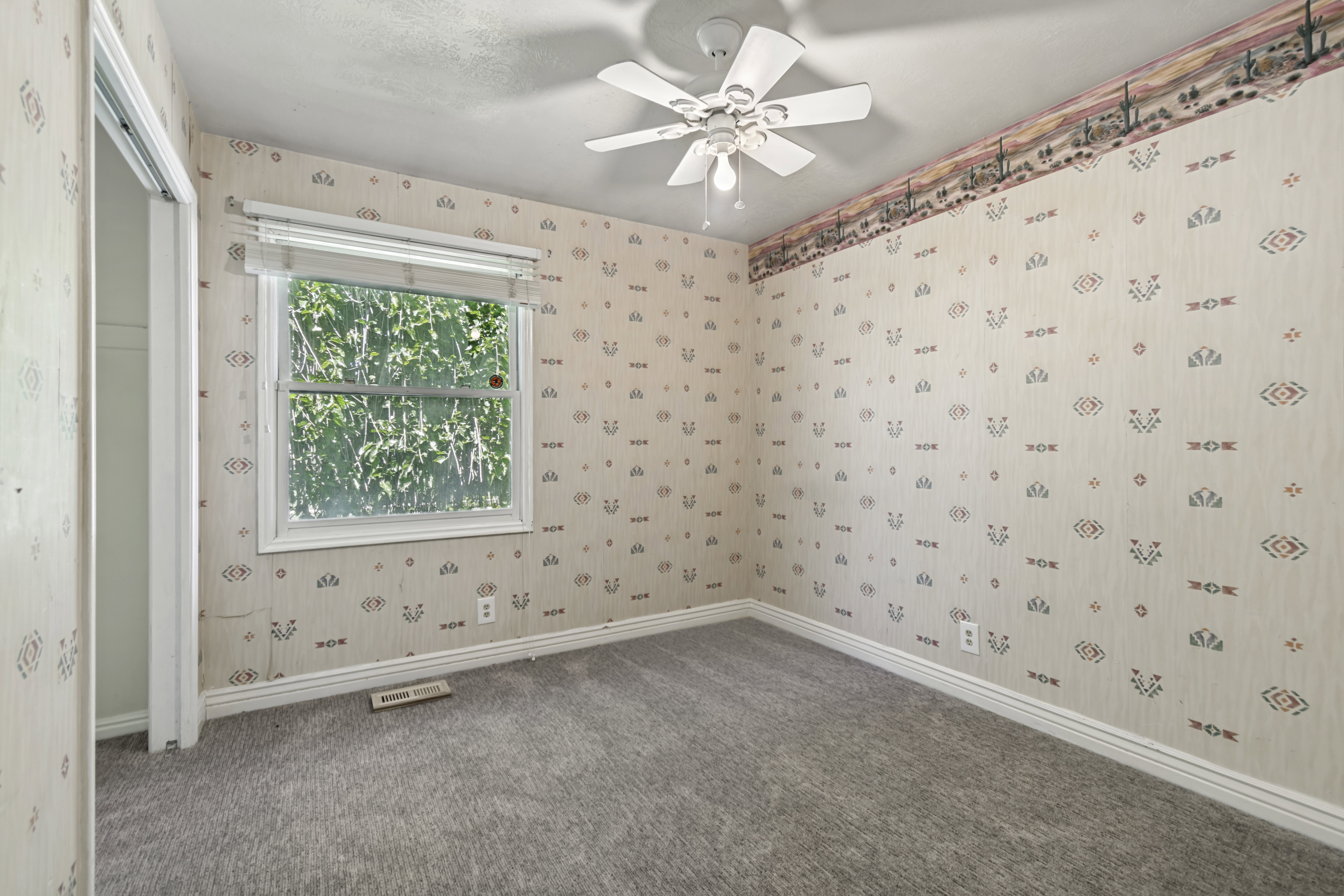 Carpeted interior room featuring a white ceiling fan, a single window, and a desert-themed border wallpaper
