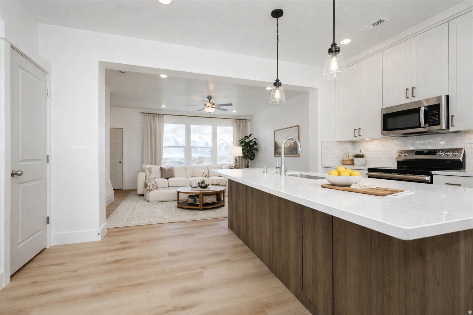Modern kitchen featuring a large island with white countertops and wood-finish paneling, stainless steel appliances, white subway tile backsplash, and light wood-finish flooring
