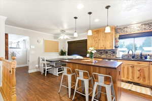 Kitchen featuring wood-finish flooring, custom wood cabinetry, a tiled backsplash, and a built-in banquette dining area