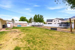 Spacious backyard featuring a large grassy area, a white privacy fence, and a brick outbuilding with an attached lean-to