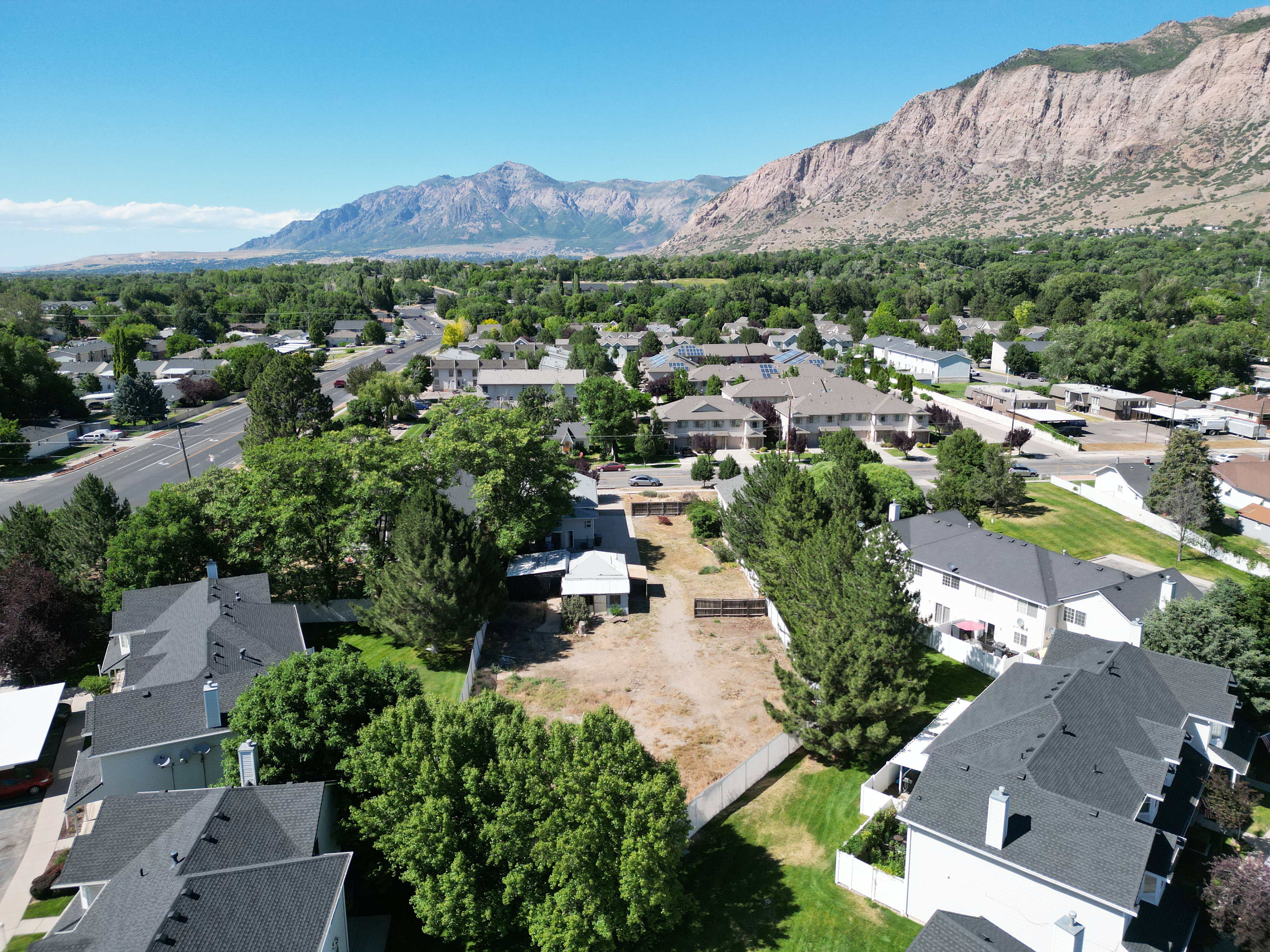 Expansive aerial perspective showcasing a residential lot with surrounding mature trees and paved roadways