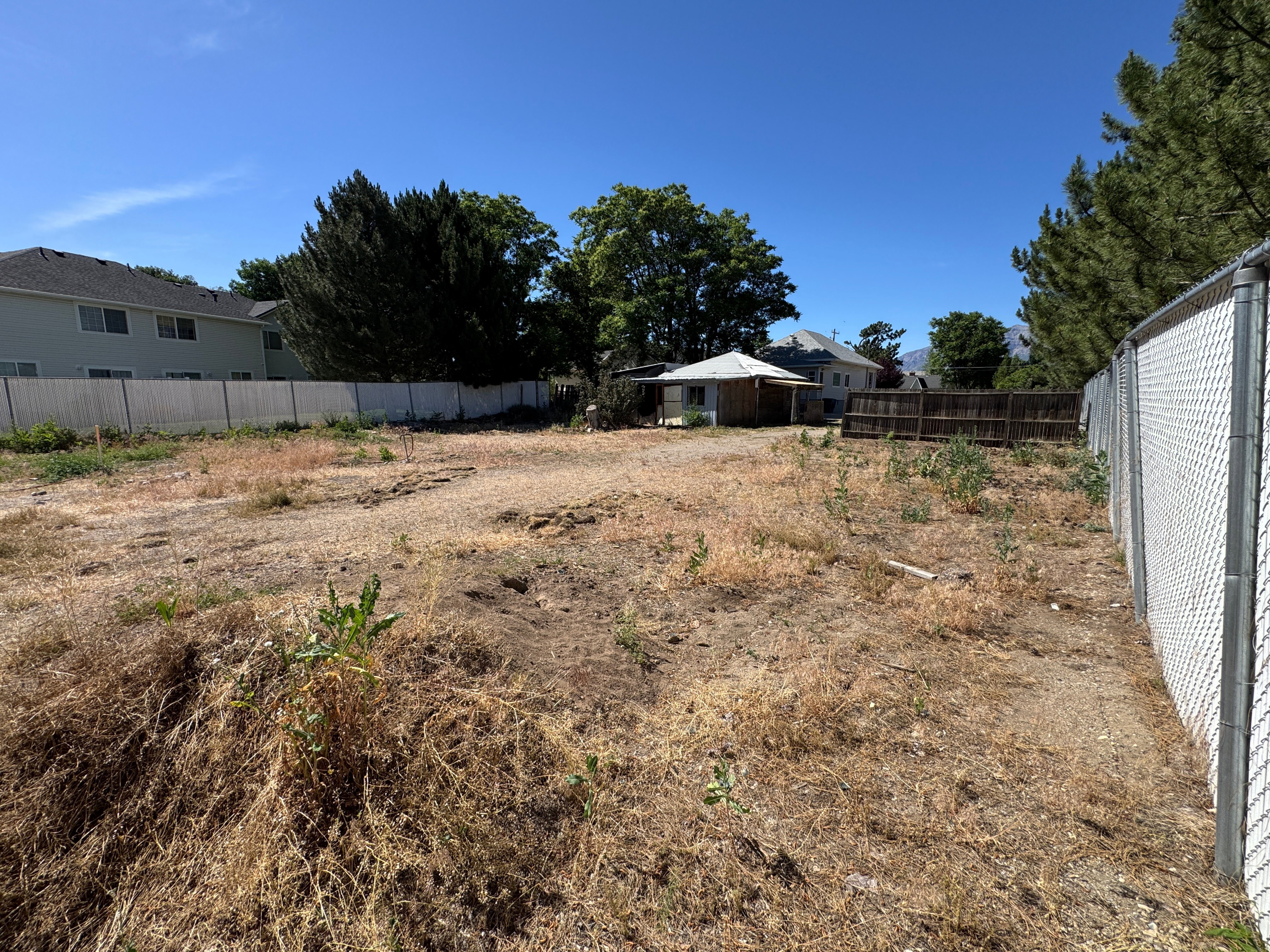 Expansive undeveloped lot featuring perimeter fencing, clear skies, and distant mountain backdrops