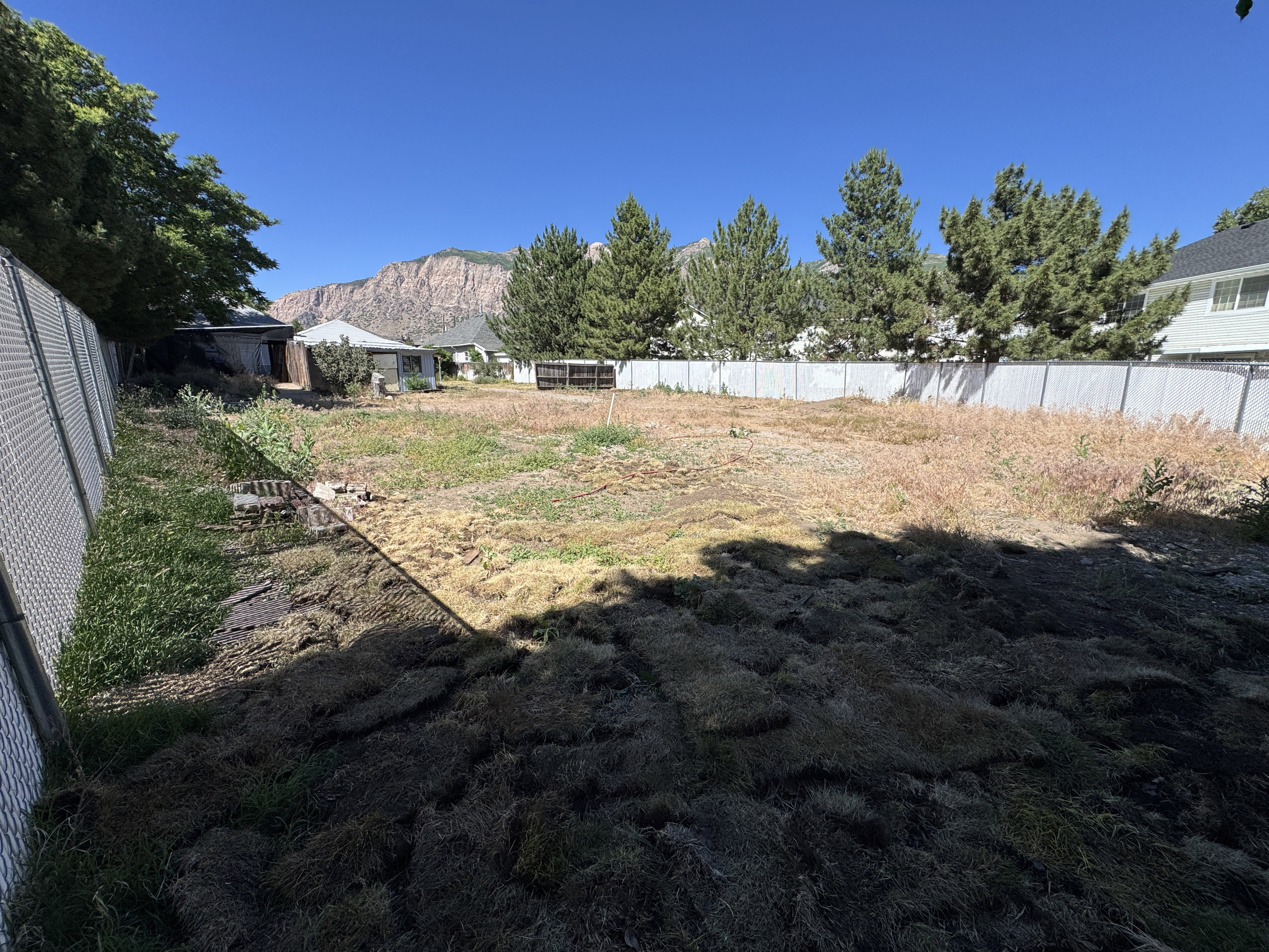 Expansive lot featuring a chain-link fence, surrounding privacy fences, mature trees, and a mountain backdrop