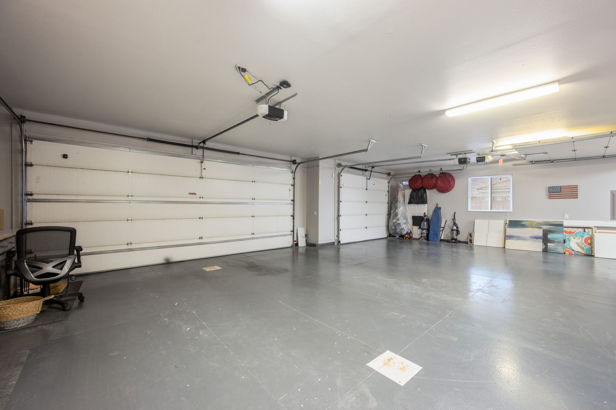 Spacious two-car garage featuring automatic door openers, overhead fluorescent lighting, and durable gray concrete flooring