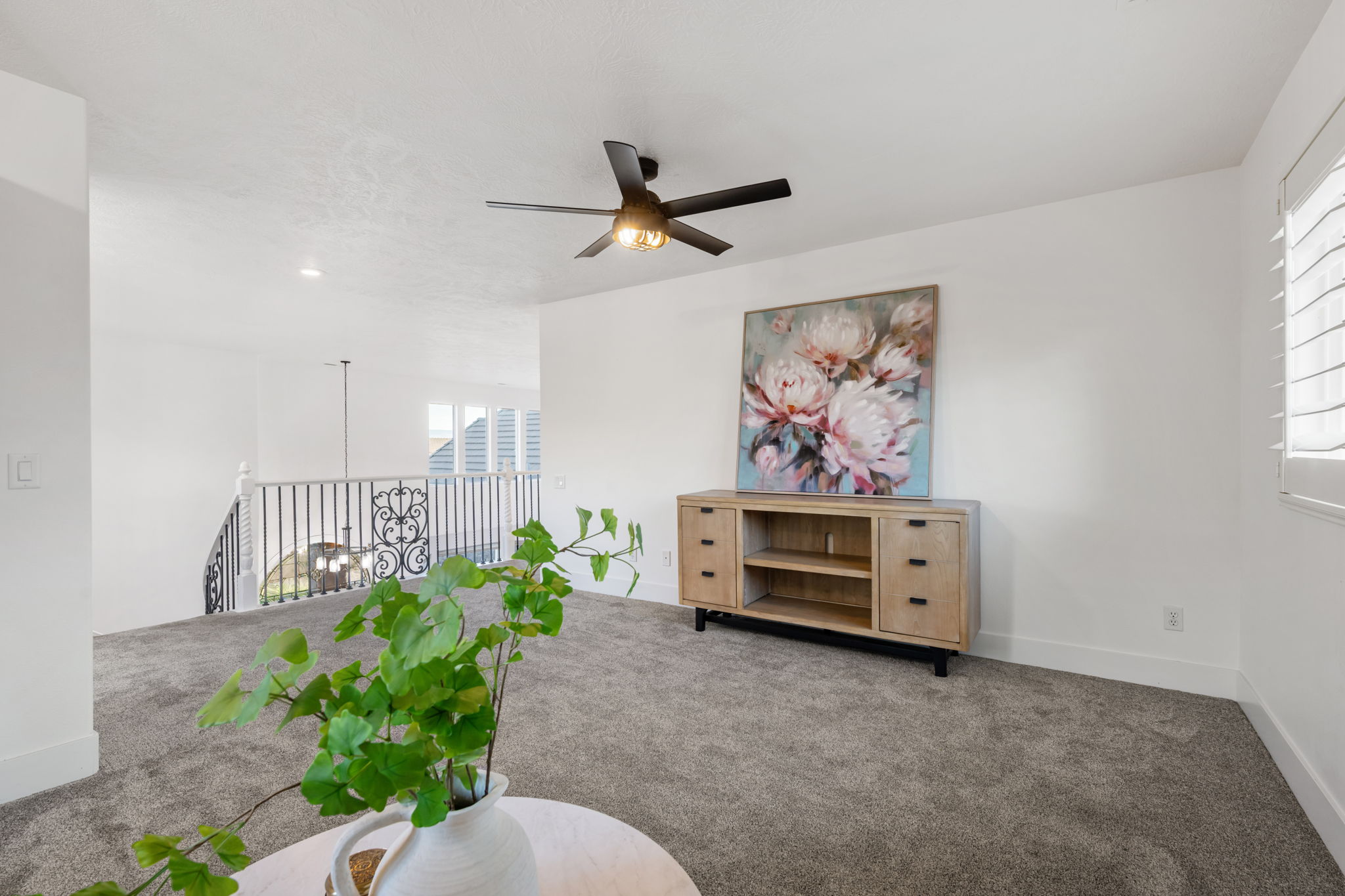 Carpeted loft area featuring a ceiling fan with integrated lighting, white walls, and a wrought iron railing overlooking the lower level