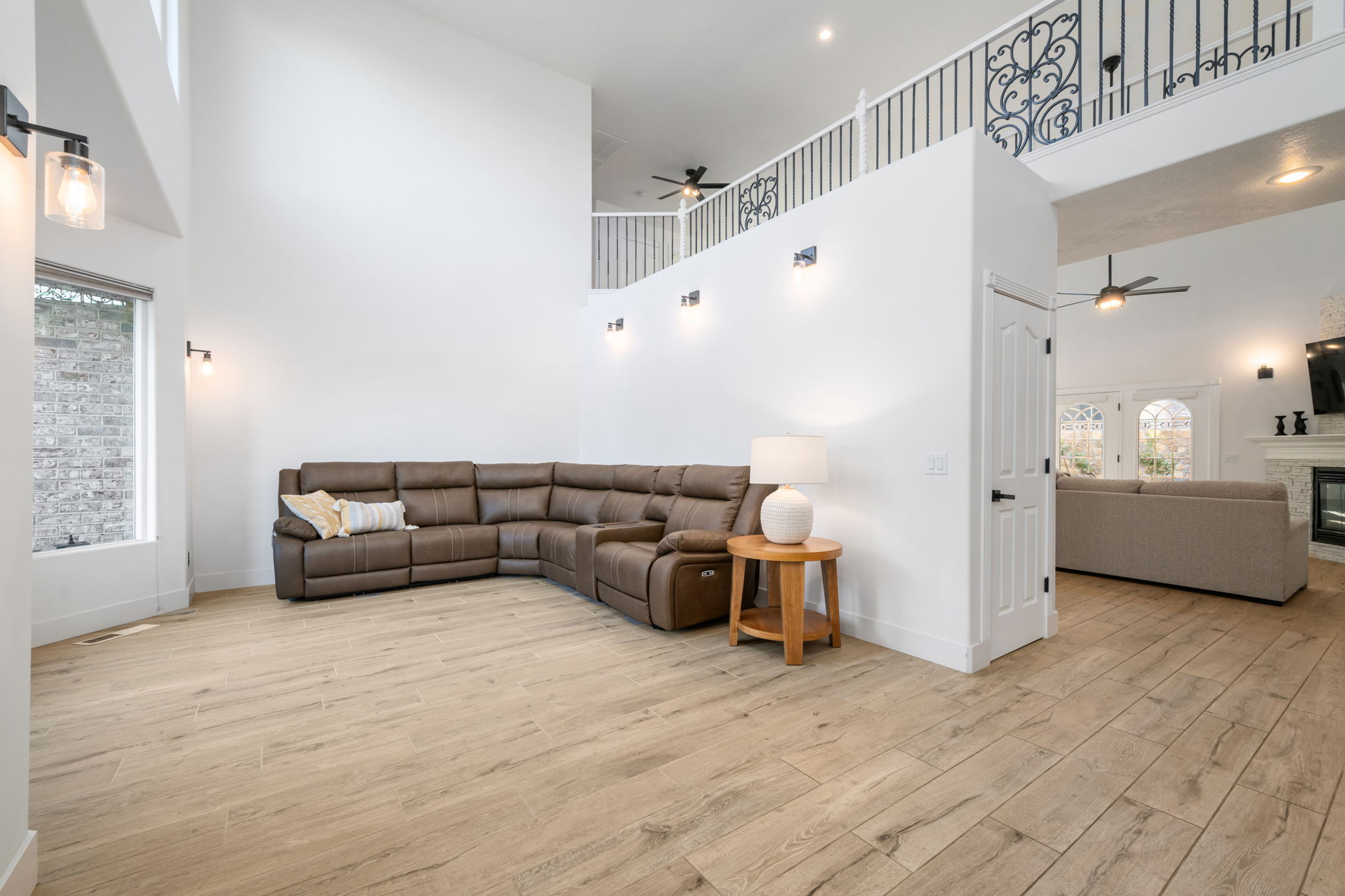 Vaulted ceiling living area featuring wood-finish flooring, a contemporary black metal and glass wall sconce, and a second-story overlook with decorative wrought iron railing