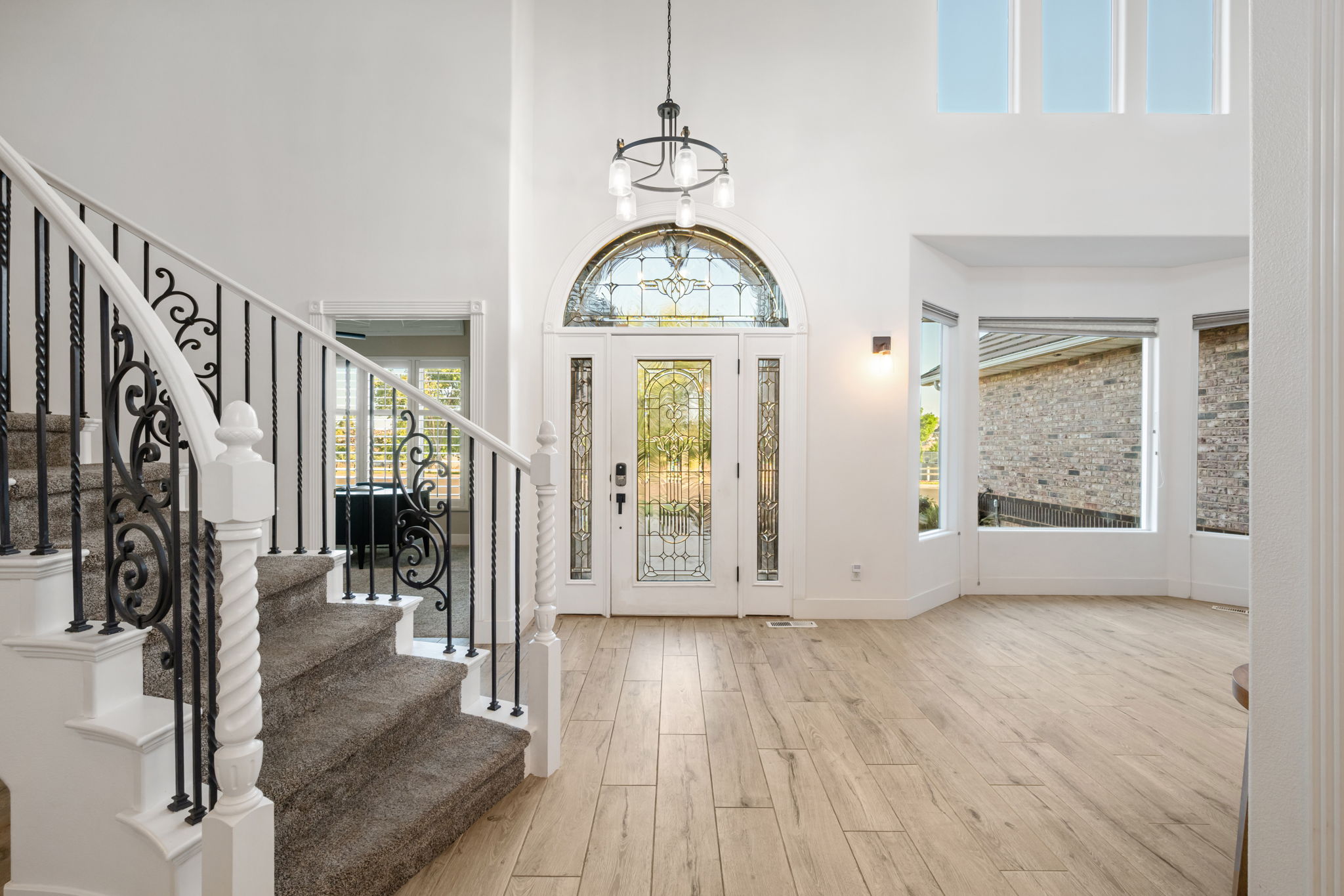 Grand entryway featuring light wood-finish flooring, a decorative stained-glass front door with transom, and a curved staircase with wrought iron balusters