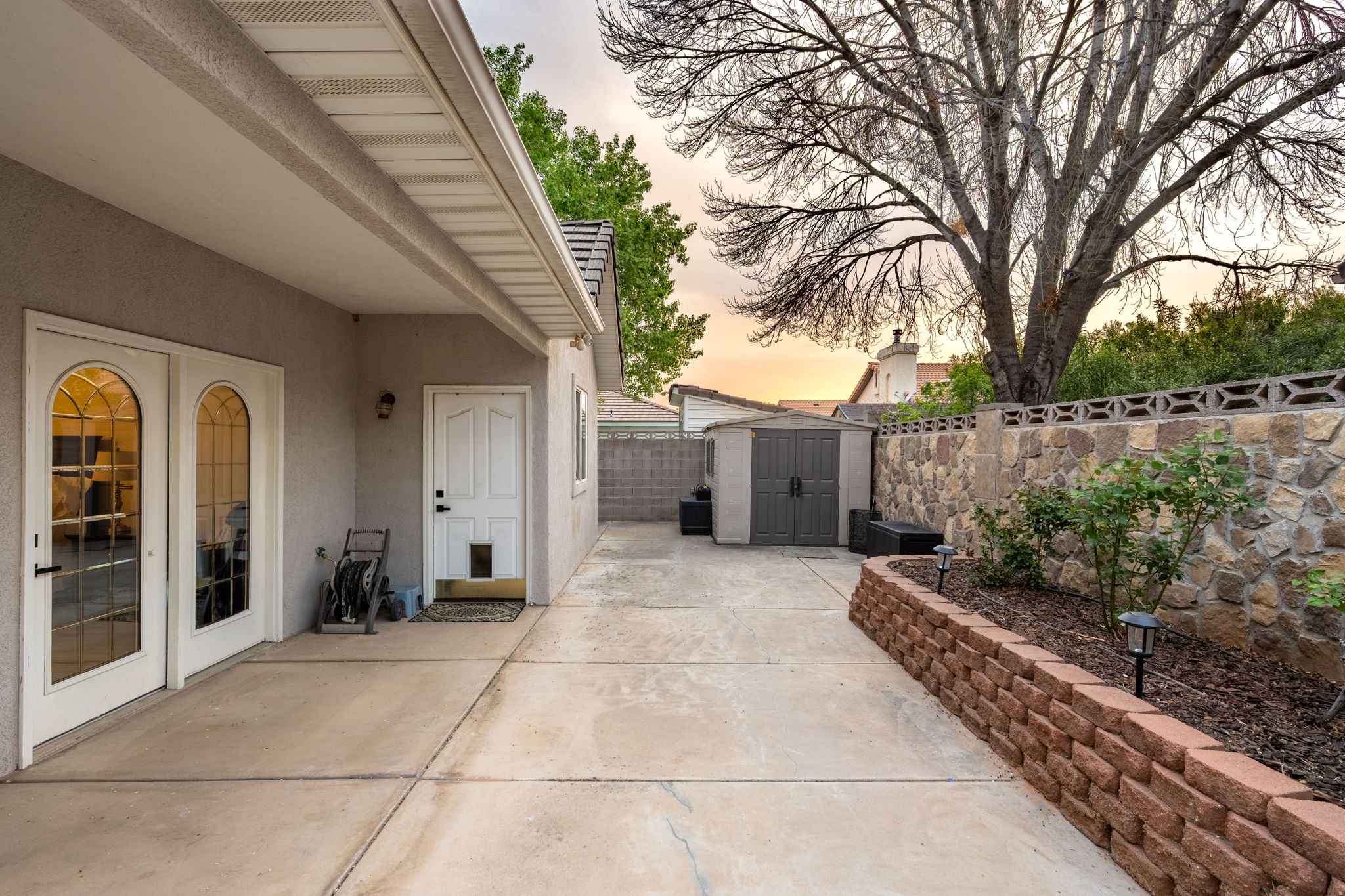 Concrete patio area featuring two arched glass-paneled doors and an exterior storage shed