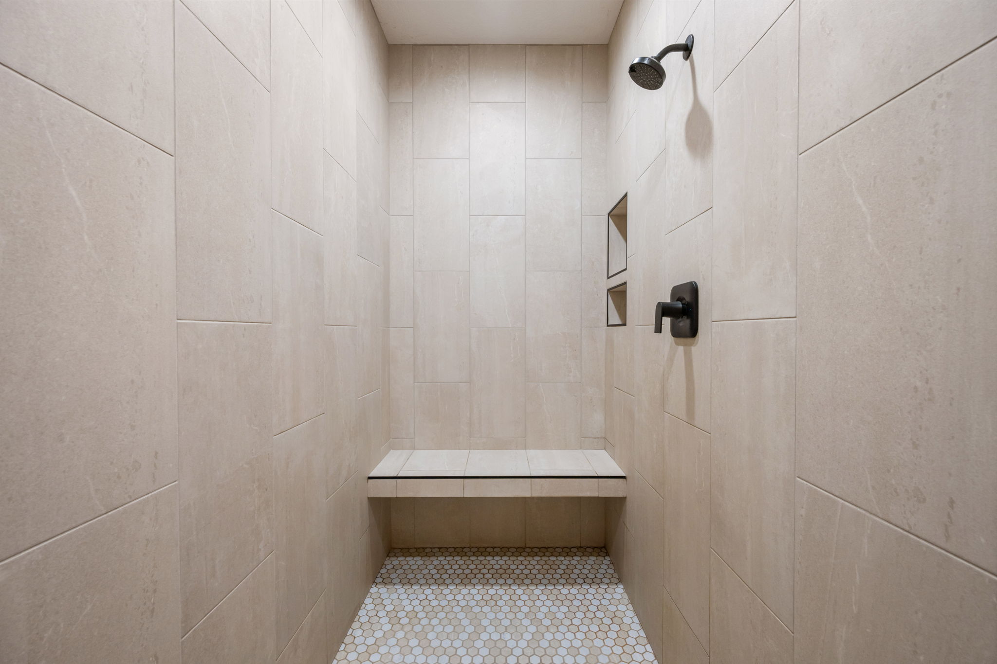 Tiled shower featuring a built-in bench, dual recessed niches, matte black shower head, and coordinating matte black single-handle control