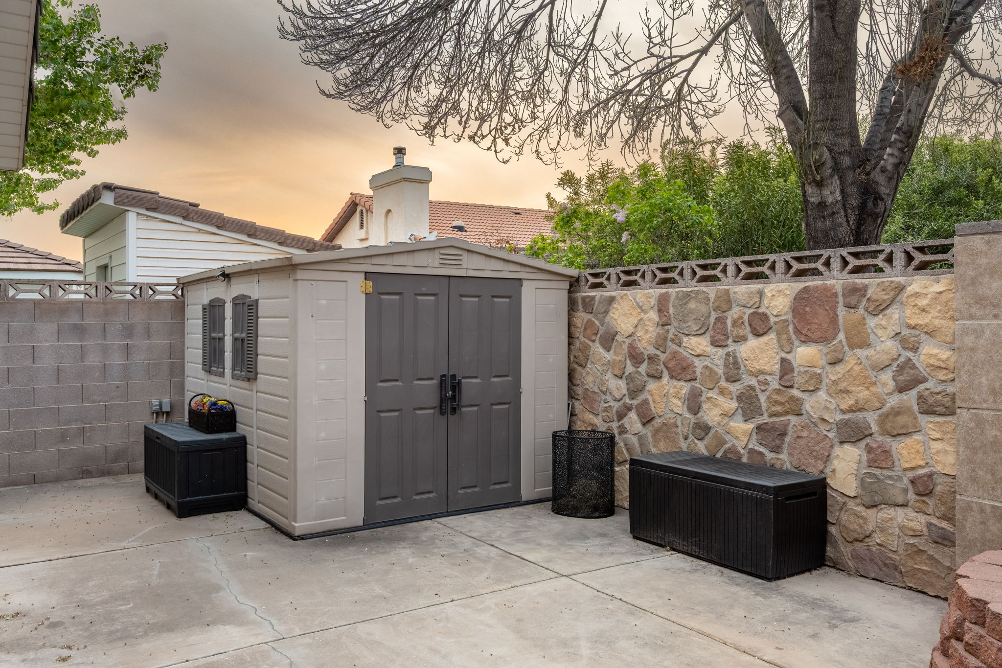 Paved outdoor area featuring a stone accent wall, a block wall, and a two-door storage shed