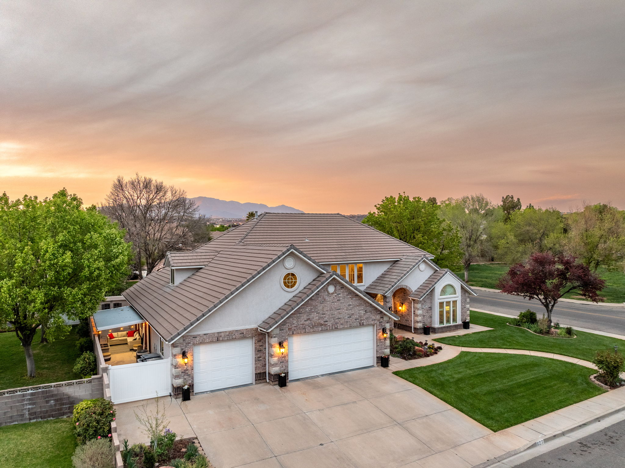 Stucco and stone facade property featuring a tile roof, an expansive driveway, and a manicured lawn