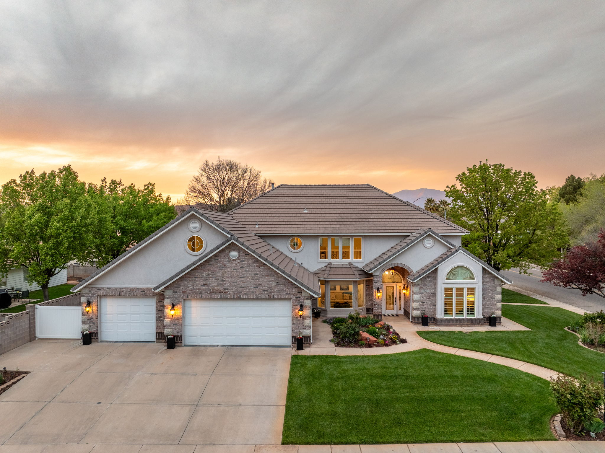 Stately residential exterior featuring an expansive concrete driveway, a manicured lawn, and mature landscaping