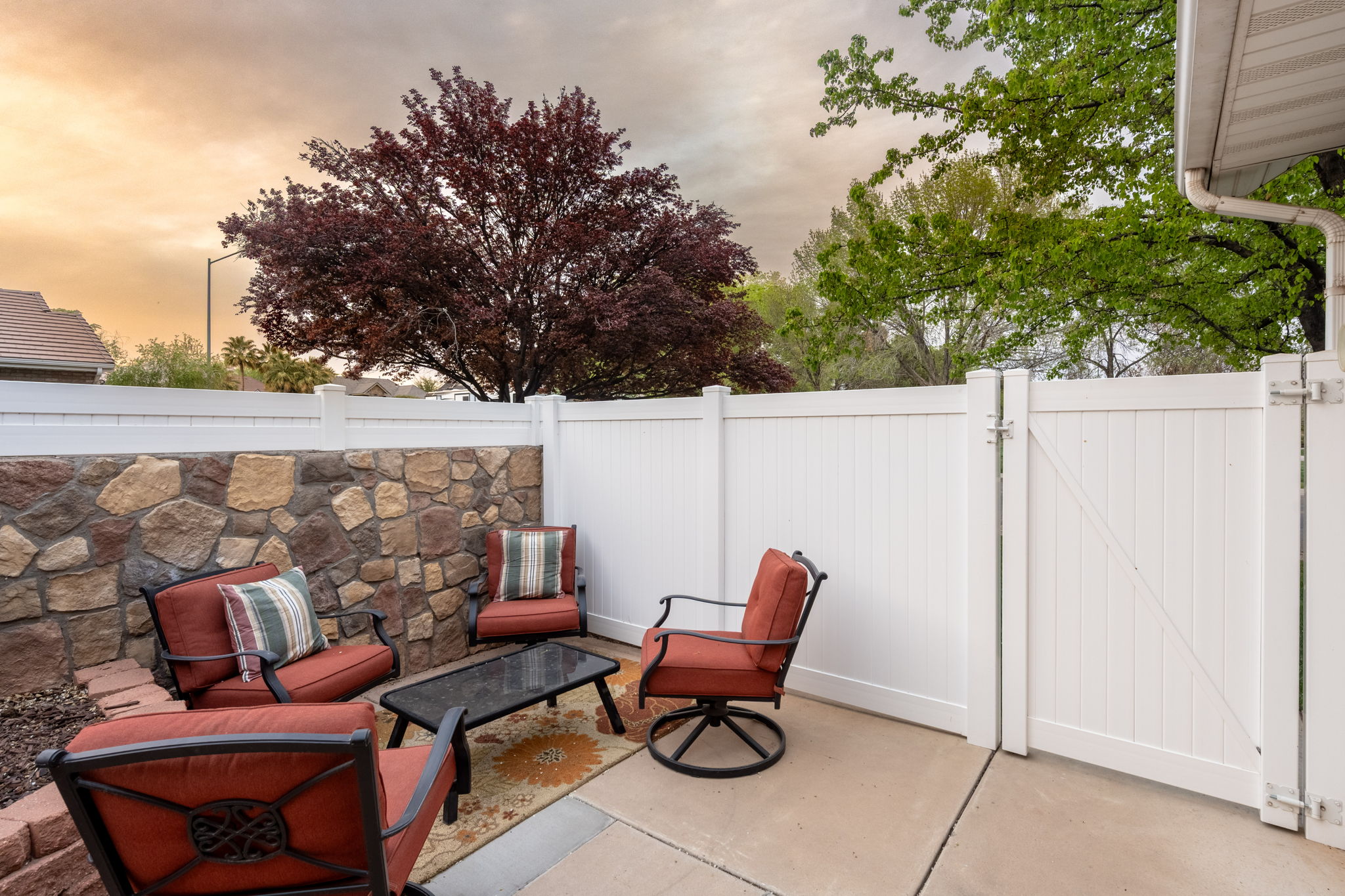 Outdoor patio featuring a stone veneer privacy wall, concrete flooring, and a white vinyl fence with a gate