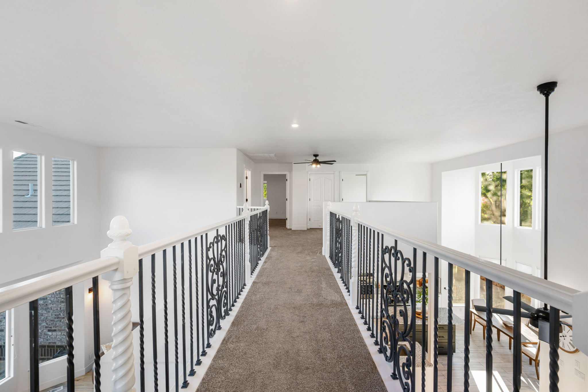 Carpeted hallway featuring white walls and ceilings, white balusters with intricate black wrought iron infill, and recessed lighting