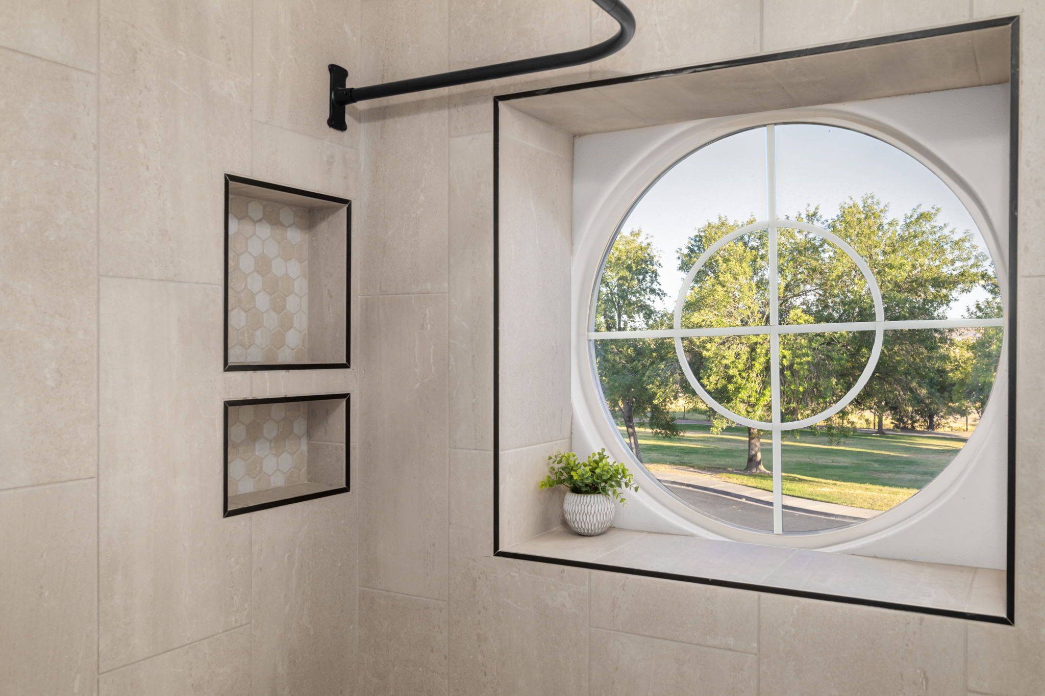 Shower featuring a circular window with decorative muntins, two recessed niches with hexagonal tile accents, and a black-finish shower rod