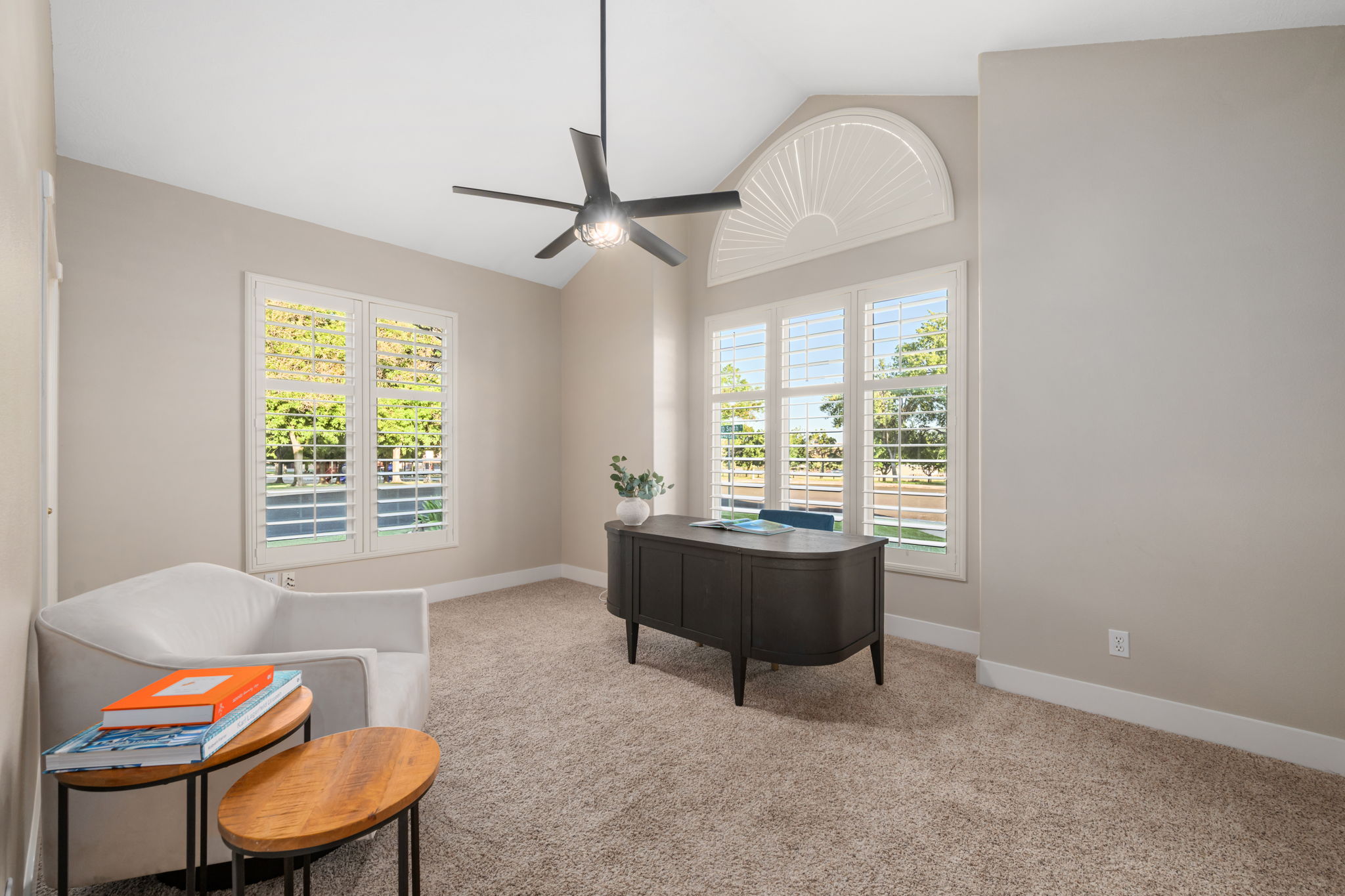 Vaulted ceiling room featuring multiple windows with plantation shutters, a decorative arched window, a contemporary ceiling fan, and neutral-toned carpeting