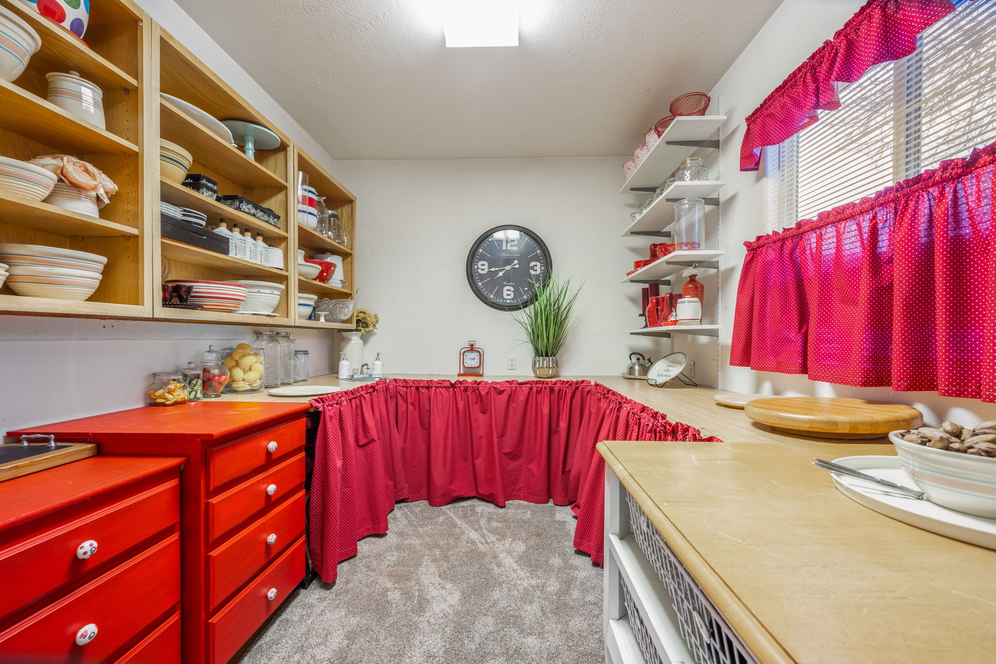 Kitchenette featuring red cabinetry with white knob hardware, light wood-finish countertops, open shelving, and a single-basin sink
