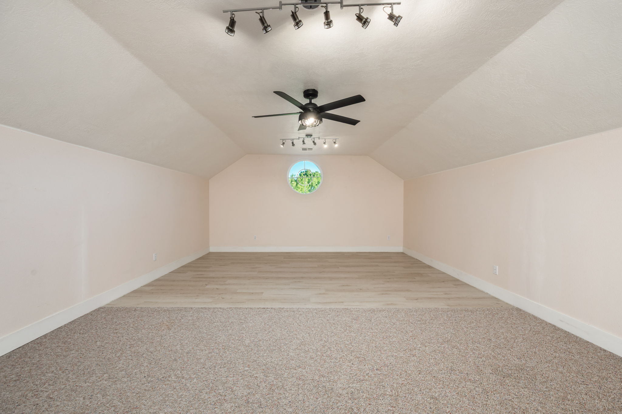 Spacious room featuring a vaulted ceiling with track lighting, a ceiling fan, and a circular window