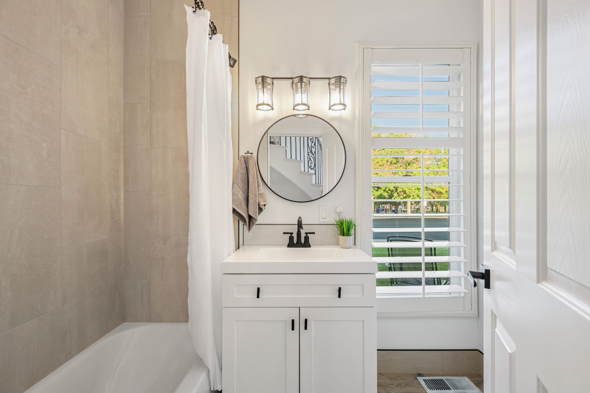 Modern bathroom featuring a white vanity with matte black hardware, a round framed mirror, and a three-light fixture