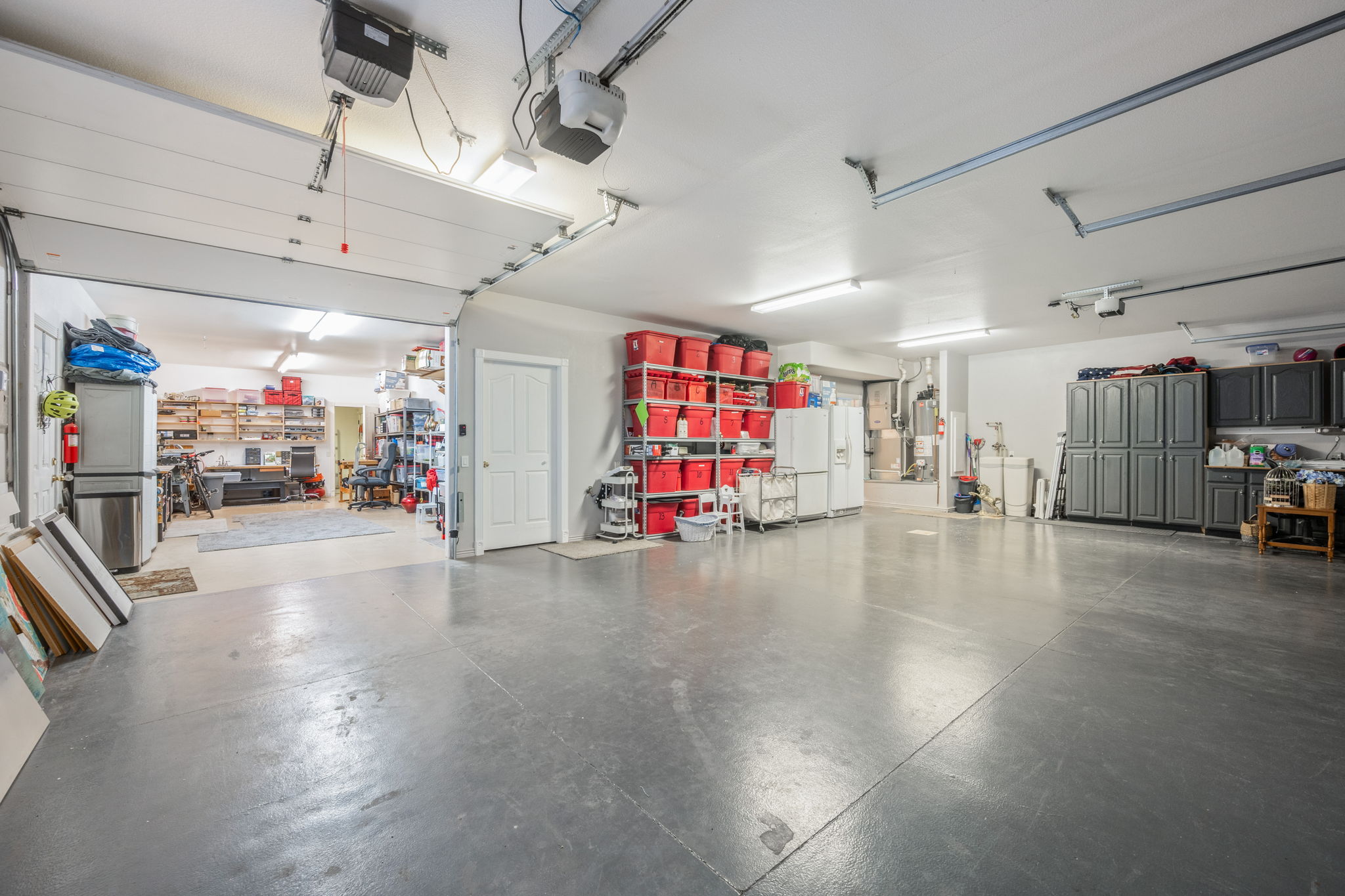 Spacious garage featuring a concrete floor, multiple overhead garage doors, built-in cabinetry, and overhead fluorescent lighting