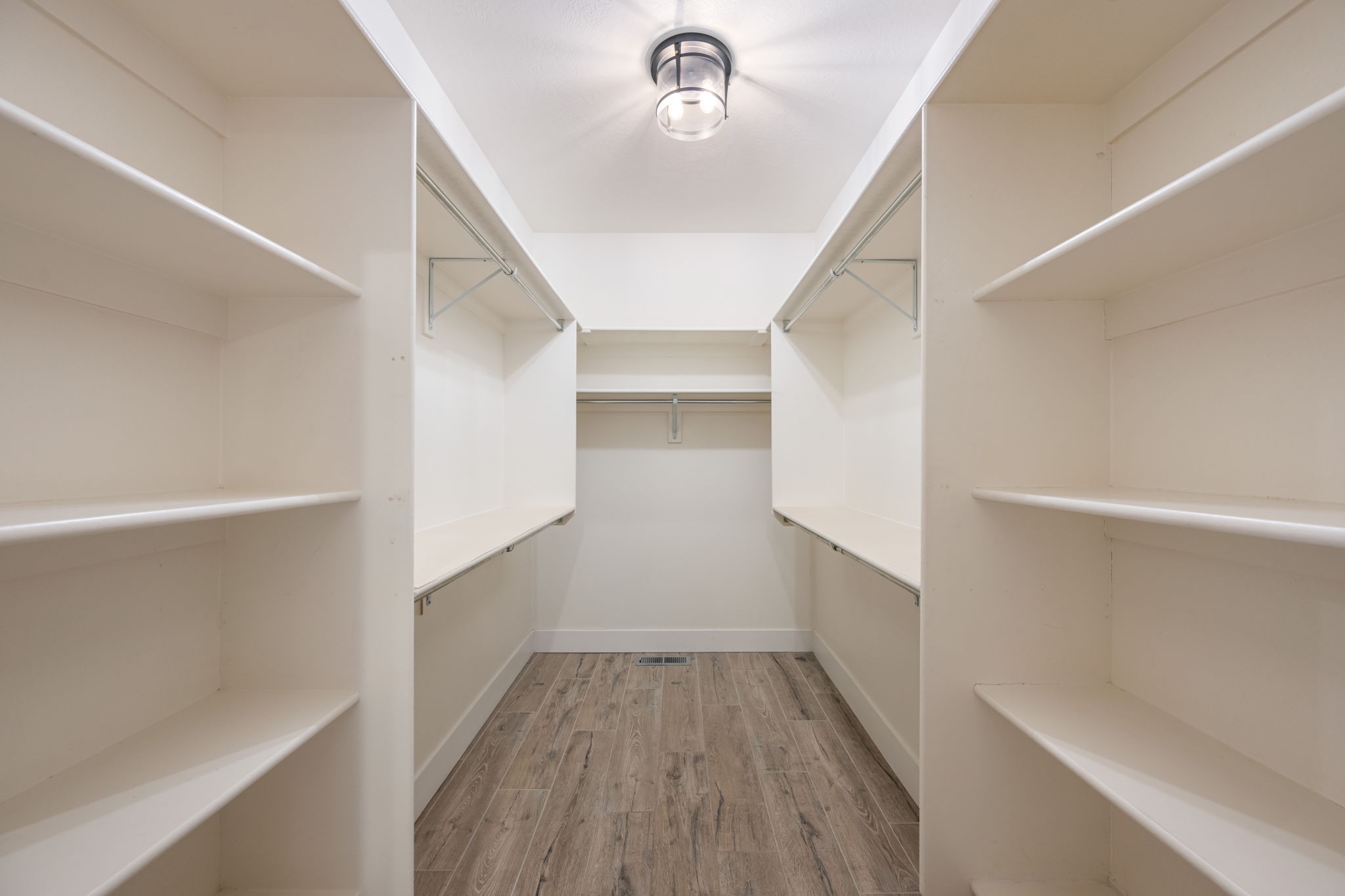 Walk-in closet featuring extensive built-in shelving, multiple hanging rods, recessed ceiling light fixture, and wood-finish flooring