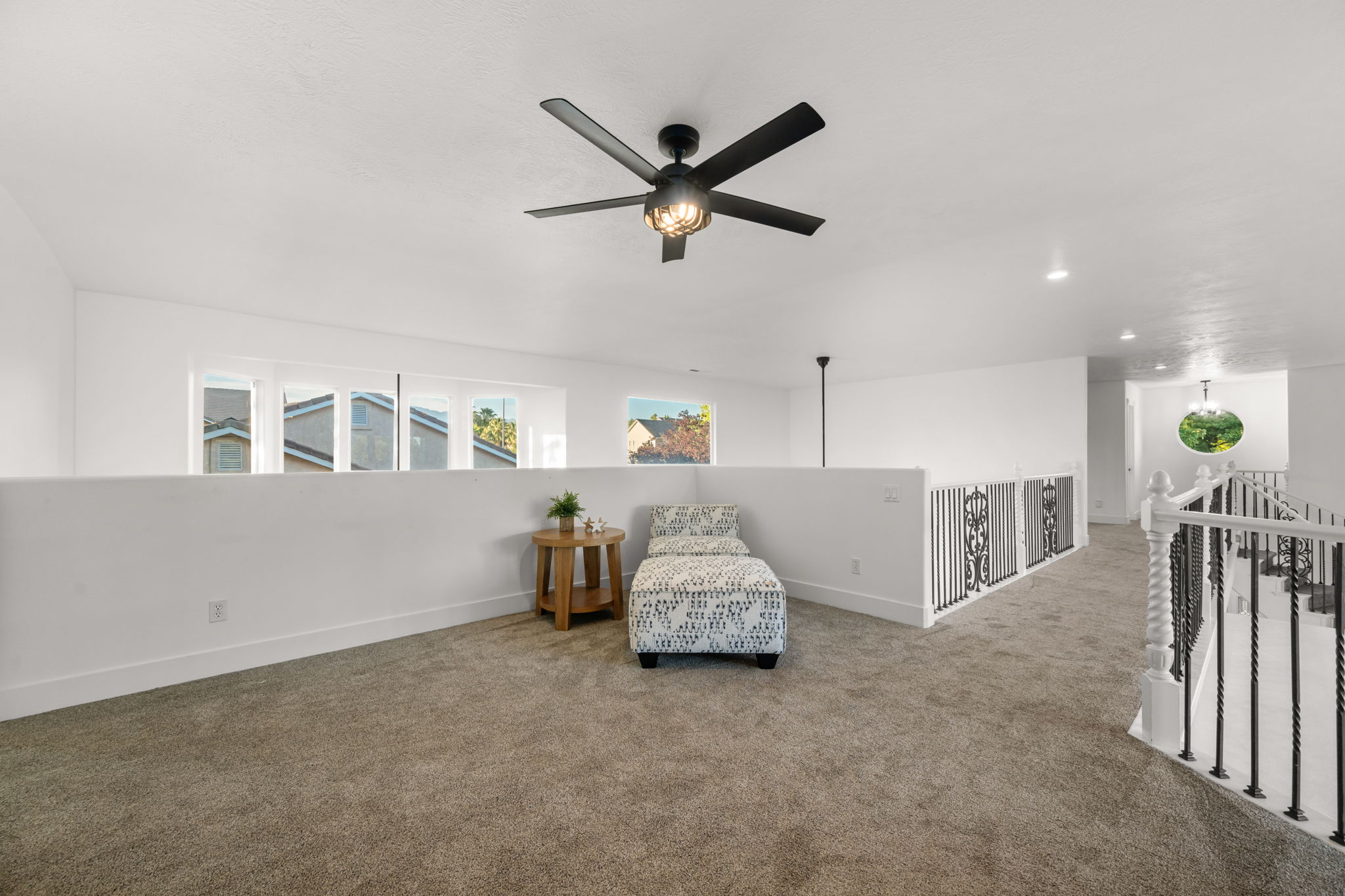 Spacious loft area featuring neutral carpeting, white walls, and a contemporary black ceiling fan with integrated lighting