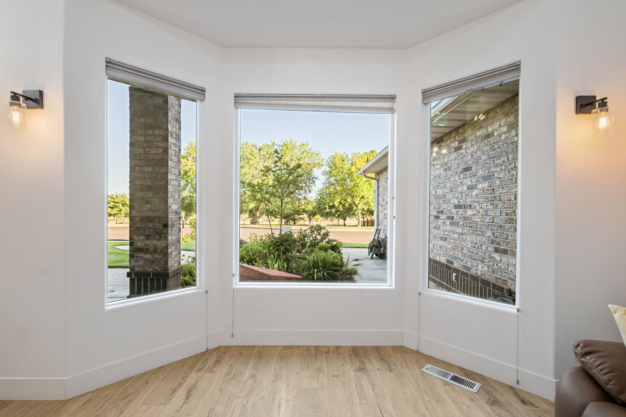 Bay window with three large windows, light wood-finish flooring, white baseboards, and two wall-mounted light fixtures