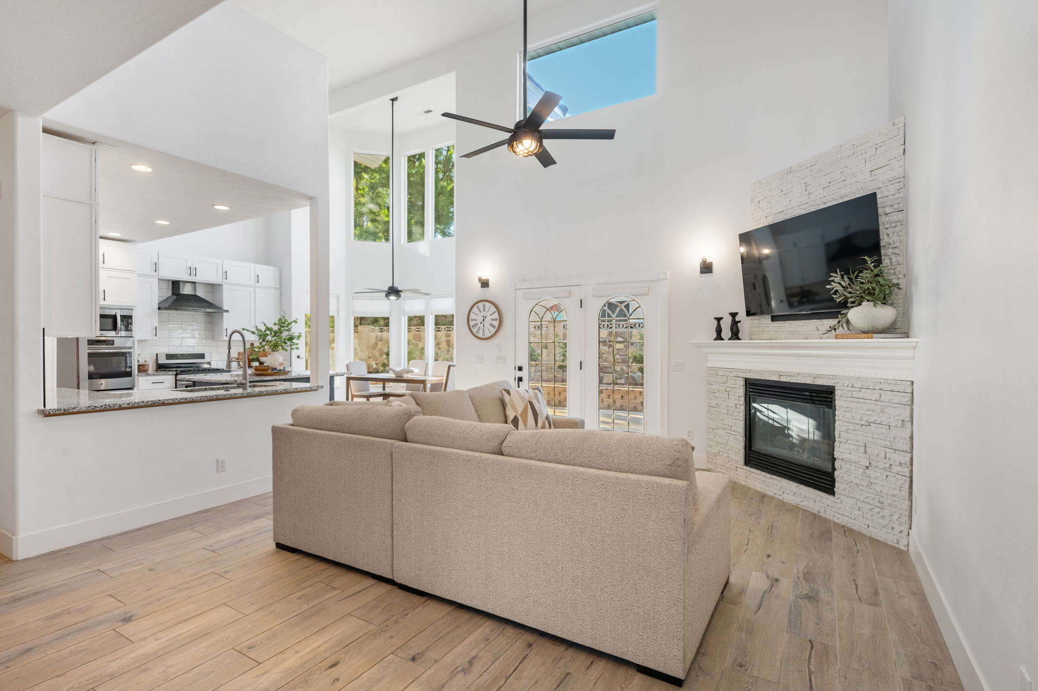 Open-concept living space featuring high ceilings with a modern ceiling fan, wood-finish flooring, a white brick-textured fireplace with a mantel, and French doors