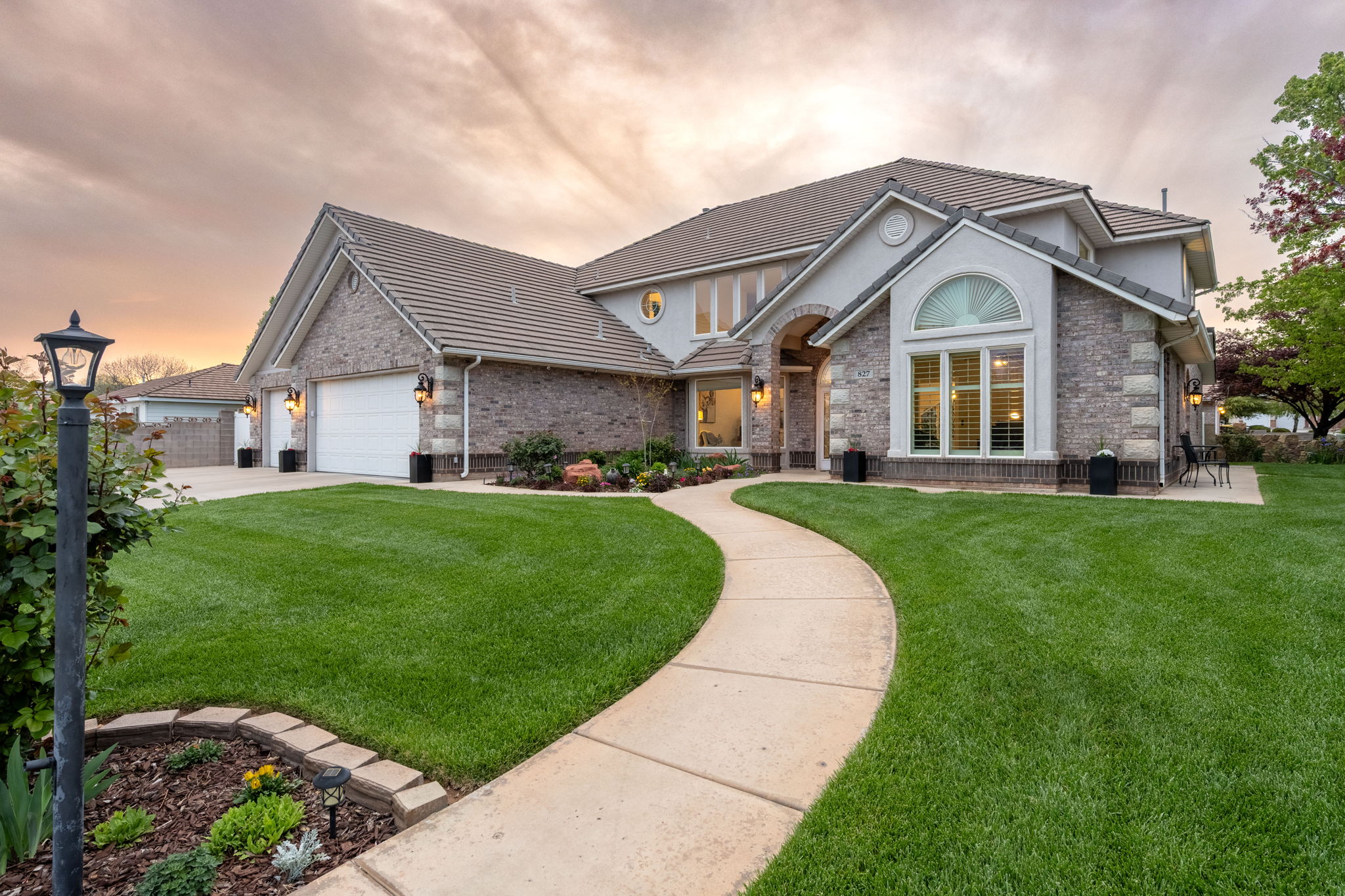 Exterior showcasing a curvilinear concrete pathway, expansive lawn, mature landscaping, and a multi-car garage