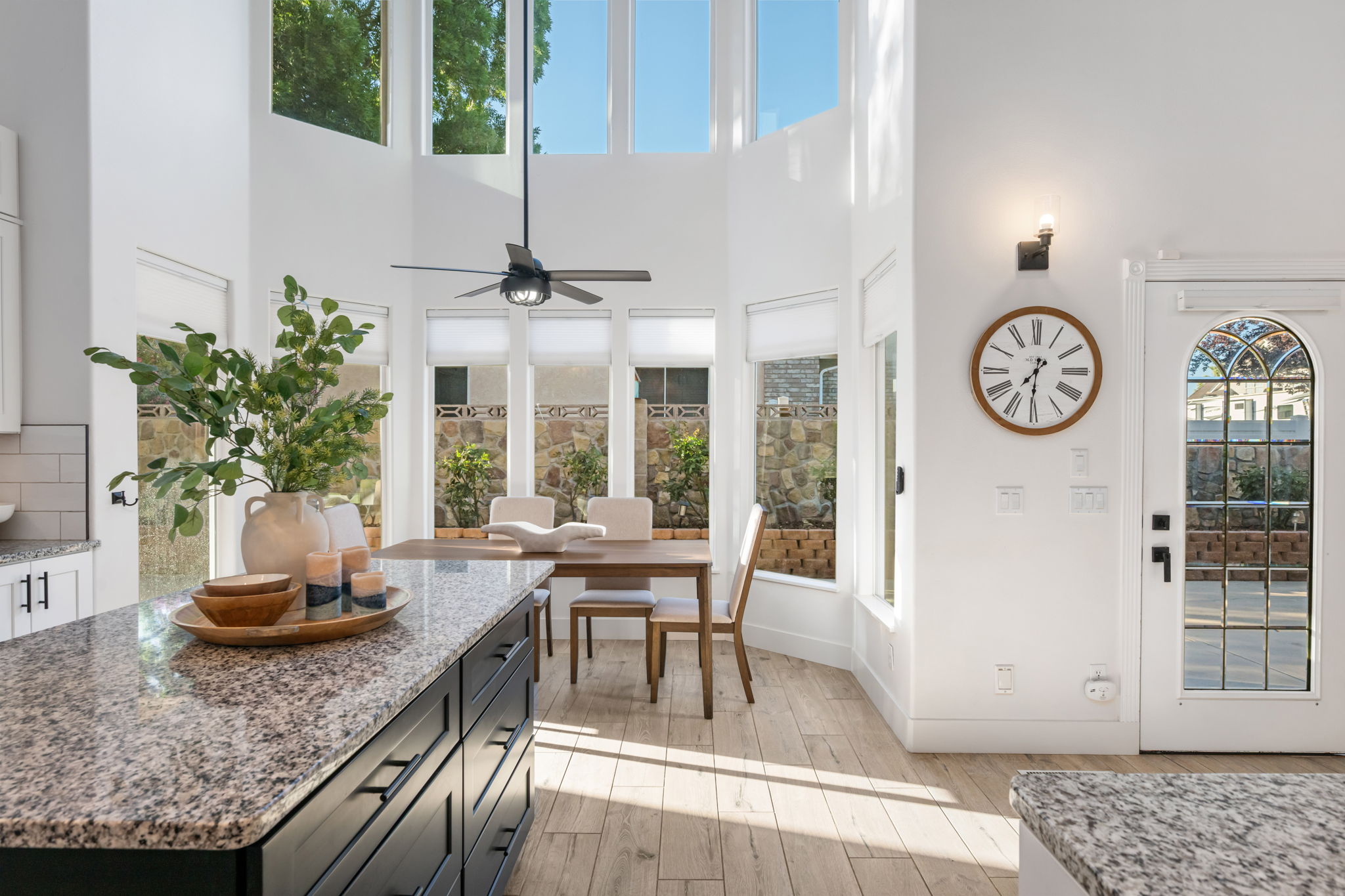 Spacious open-concept area featuring a large kitchen island with a speckled countertop, a dining area with expansive windows, and a high ceiling with a ceiling fan